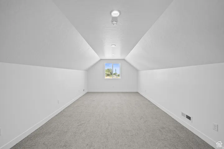Attic room featuring a window, recessed lighting, white walls, angled ceilings, and grey carpeting