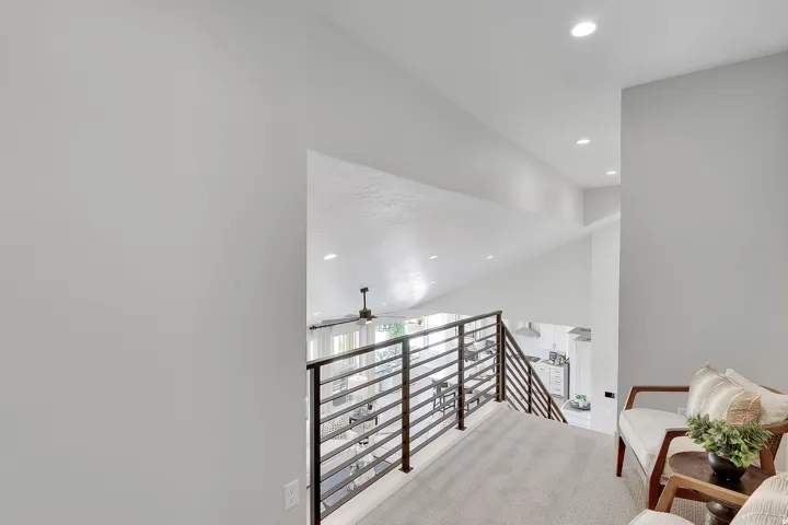 Upper-level landing featuring a wood-finish and metal horizontal railing system, recessed lighting, and a vaulted ceiling