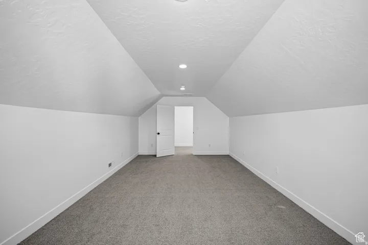 Spacious room featuring vaulted ceilings, recessed lighting, neutral wall paint, and gray carpeting