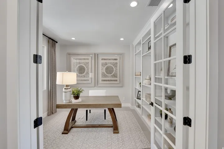 French doors opening to a dedicated office space featuring built-in shelving, recessed lighting, and a large window