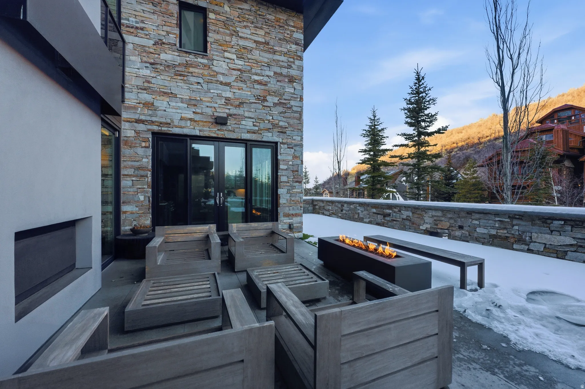 Stone-clad exterior featuring a spacious patio with a built-in linear fire pit
