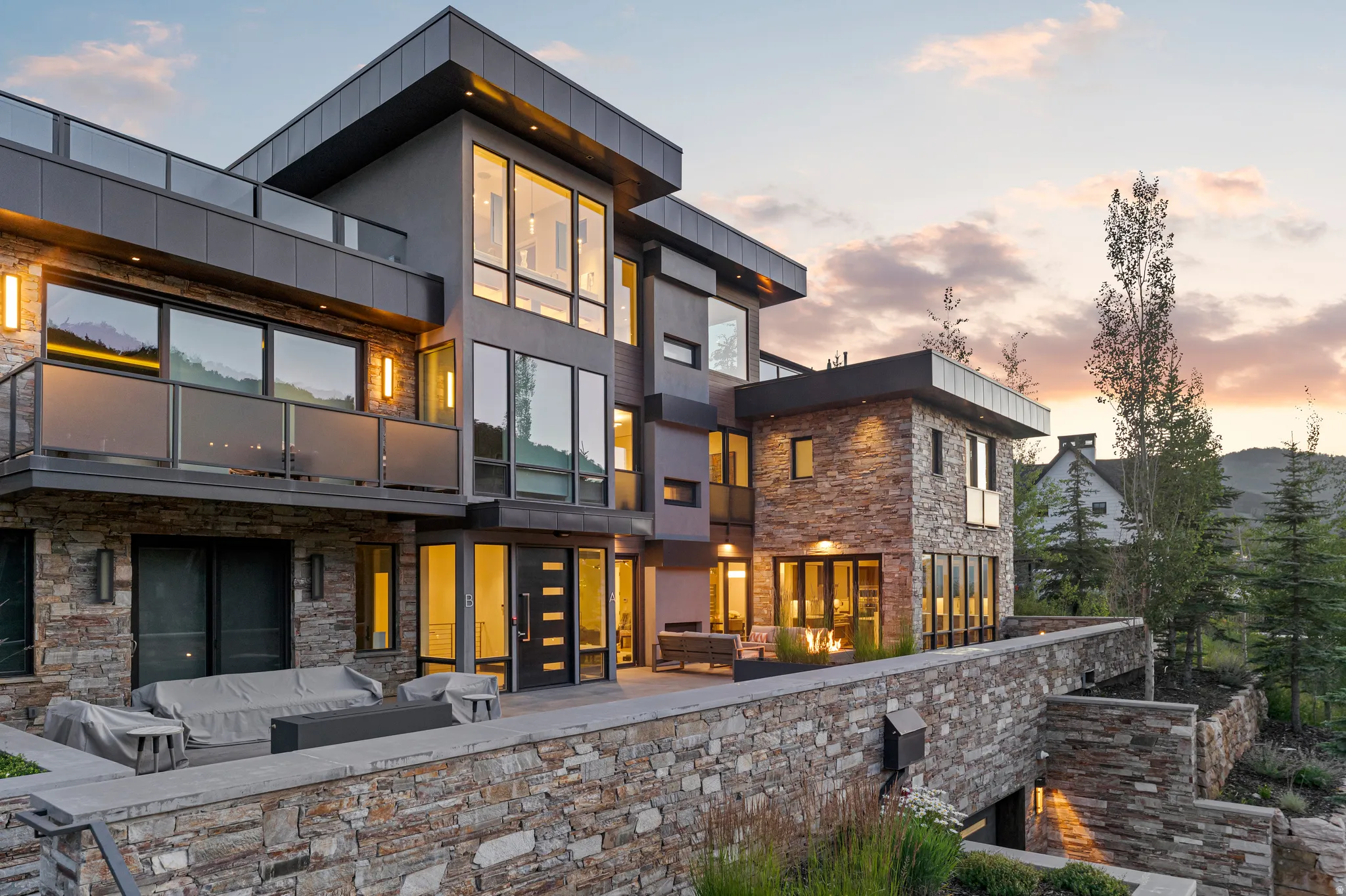 Contemporary facade featuring extensive stone cladding, large format windows, a flat roofline, multiple balconies with glass railings, and an integrated outdoor patio