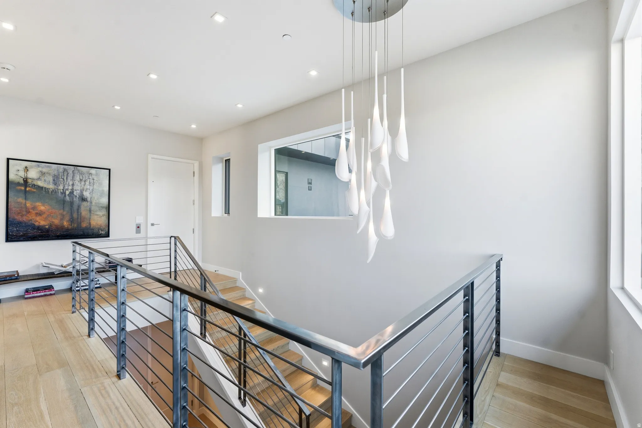 Modern staircase featuring a sleek metal railing with horizontal balusters, wood-finish flooring, and recessed ceiling lighting