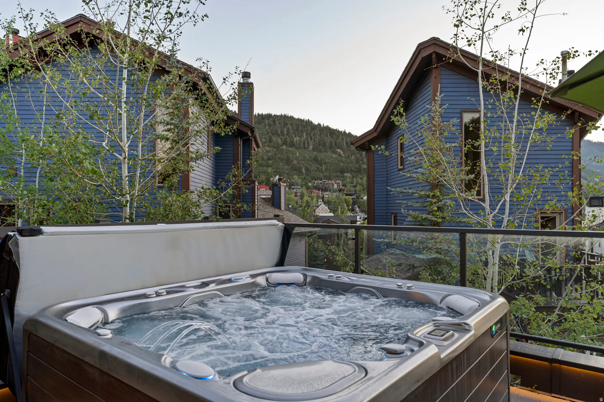 Outdoor hot tub with integrated jets and controls, set on a deck with glass panel railing