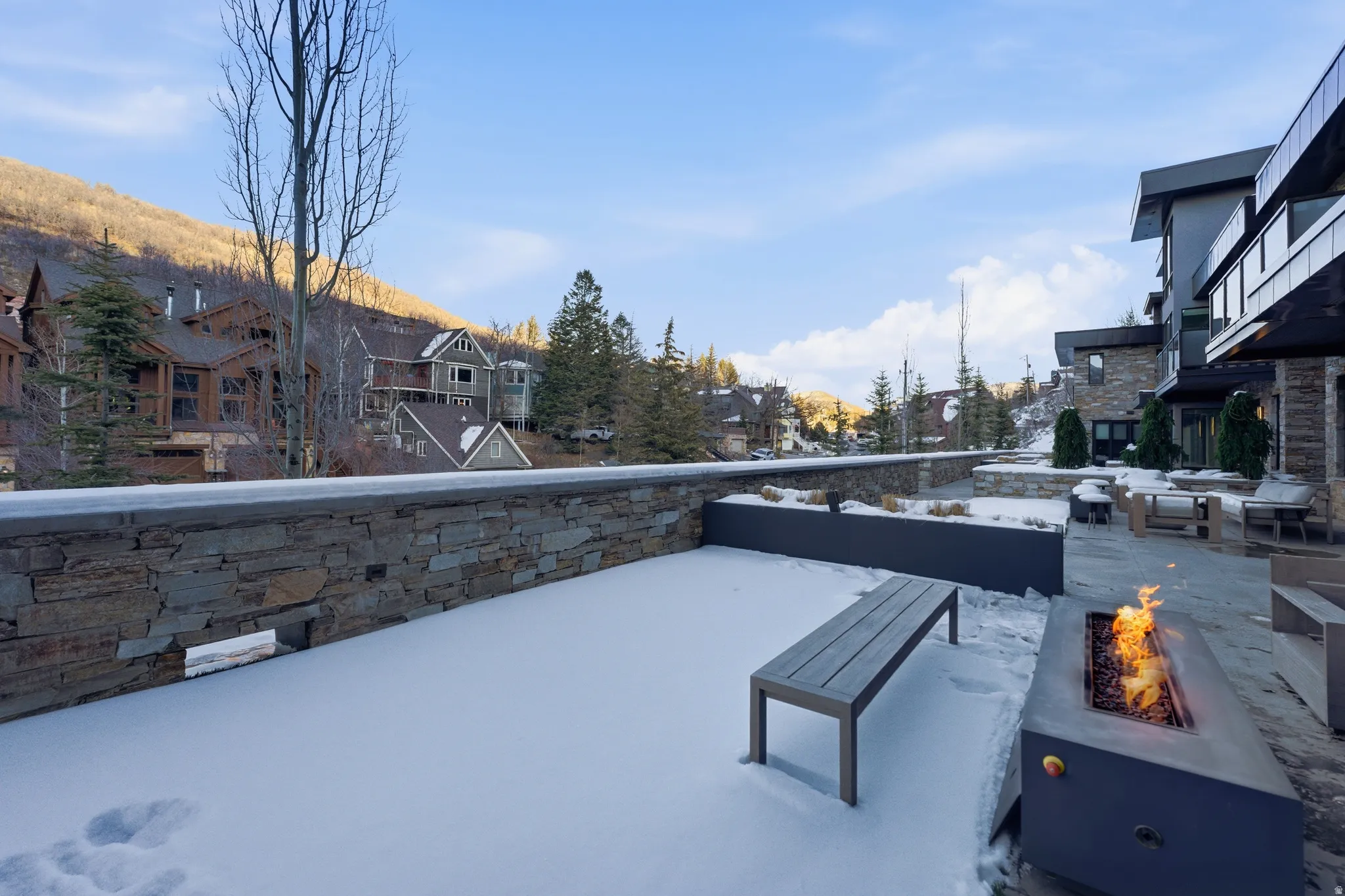 Expansive outdoor patio featuring a linear fire pit, stone accent wall, and mountain scenery
