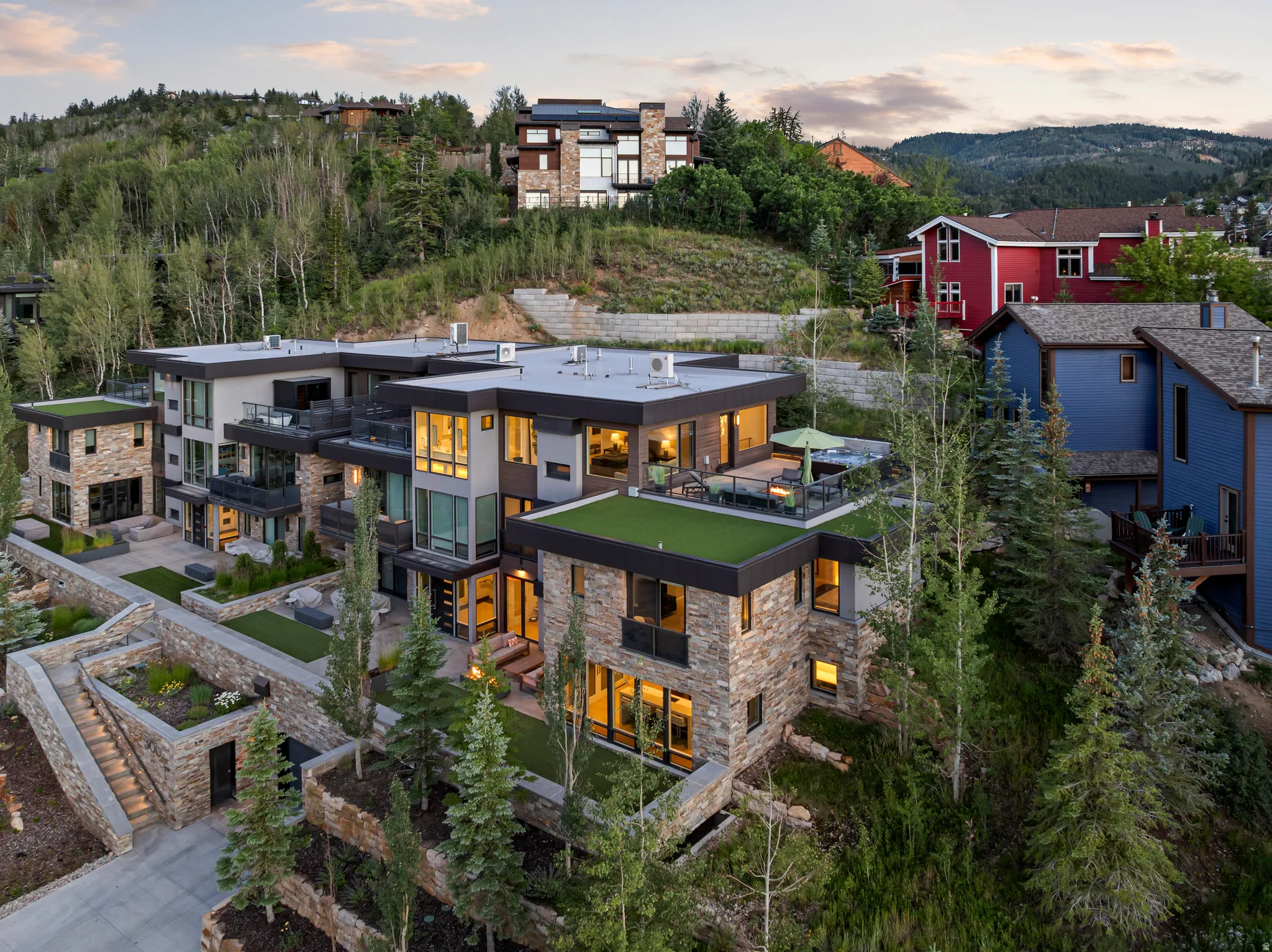 Contemporary multi-level residence featuring stone and stucco facade, multiple exterior terraces, green roof accents, and landscaped grounds with mature trees