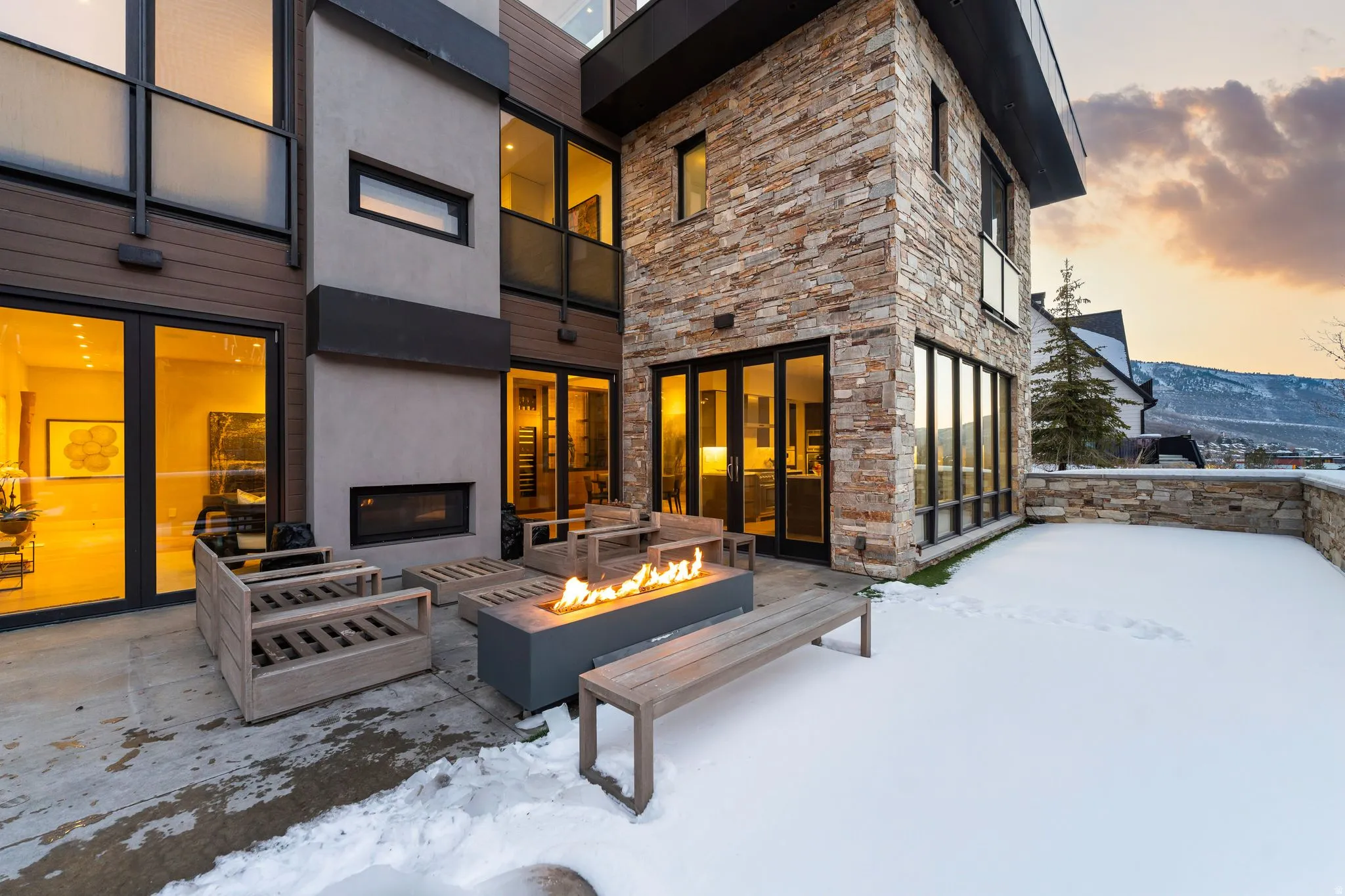 Expansive patio featuring an integrated gas fire pit, built-in outdoor fireplace, and multiple floor-to-ceiling glass doors