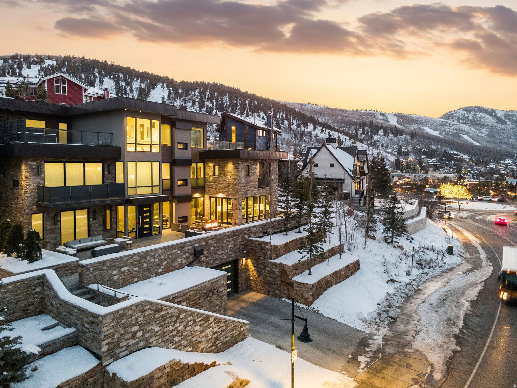Modern multi-level exterior featuring extensive glass windows, stone veneer accents, multiple balconies with glass railings, and a tiered stone retaining wall system