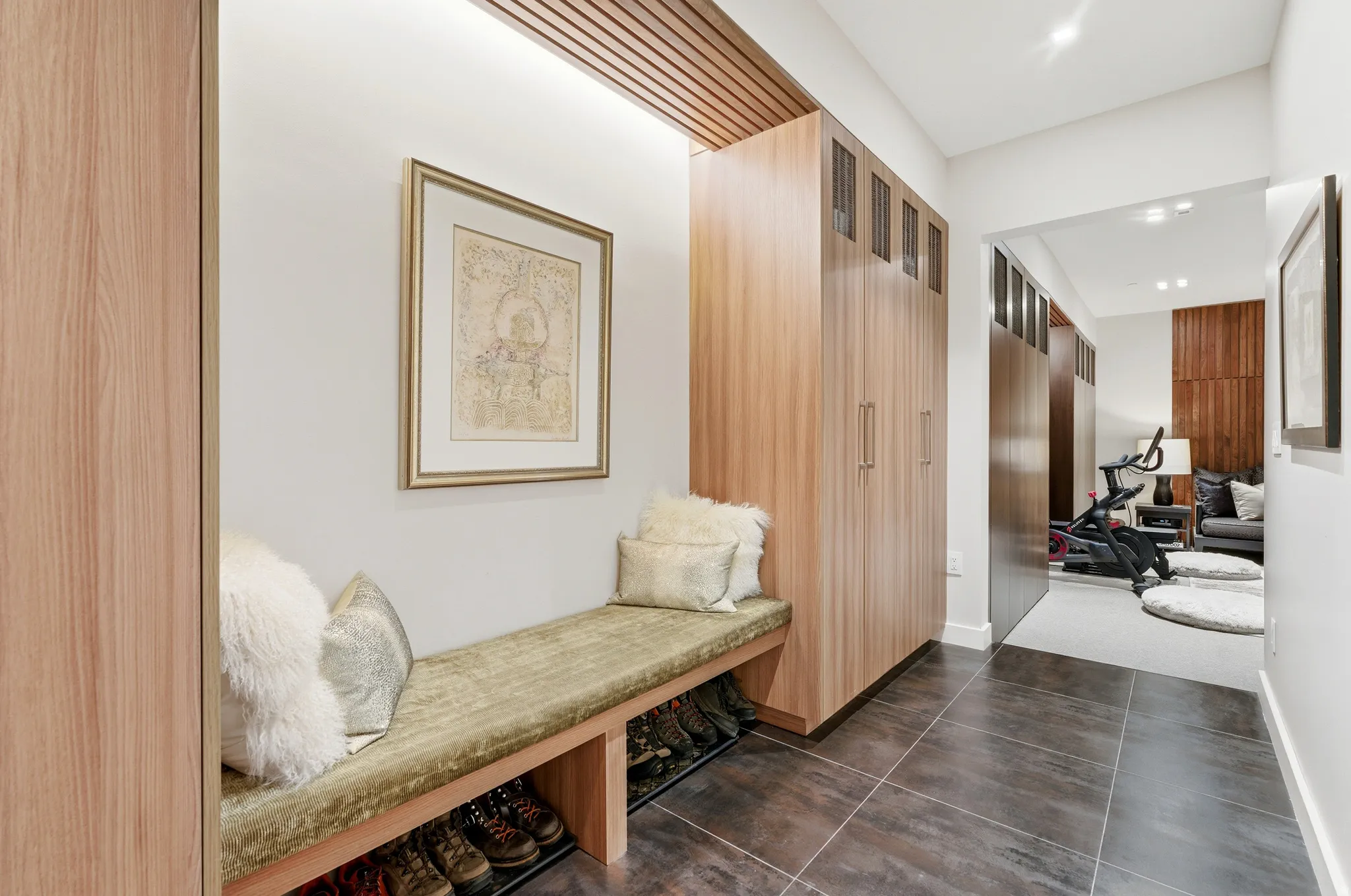 Entryway featuring a built-in upholstered bench with integrated shoe storage, wood-finish cabinetry with silver-tone hardware, and recessed ceiling lighting