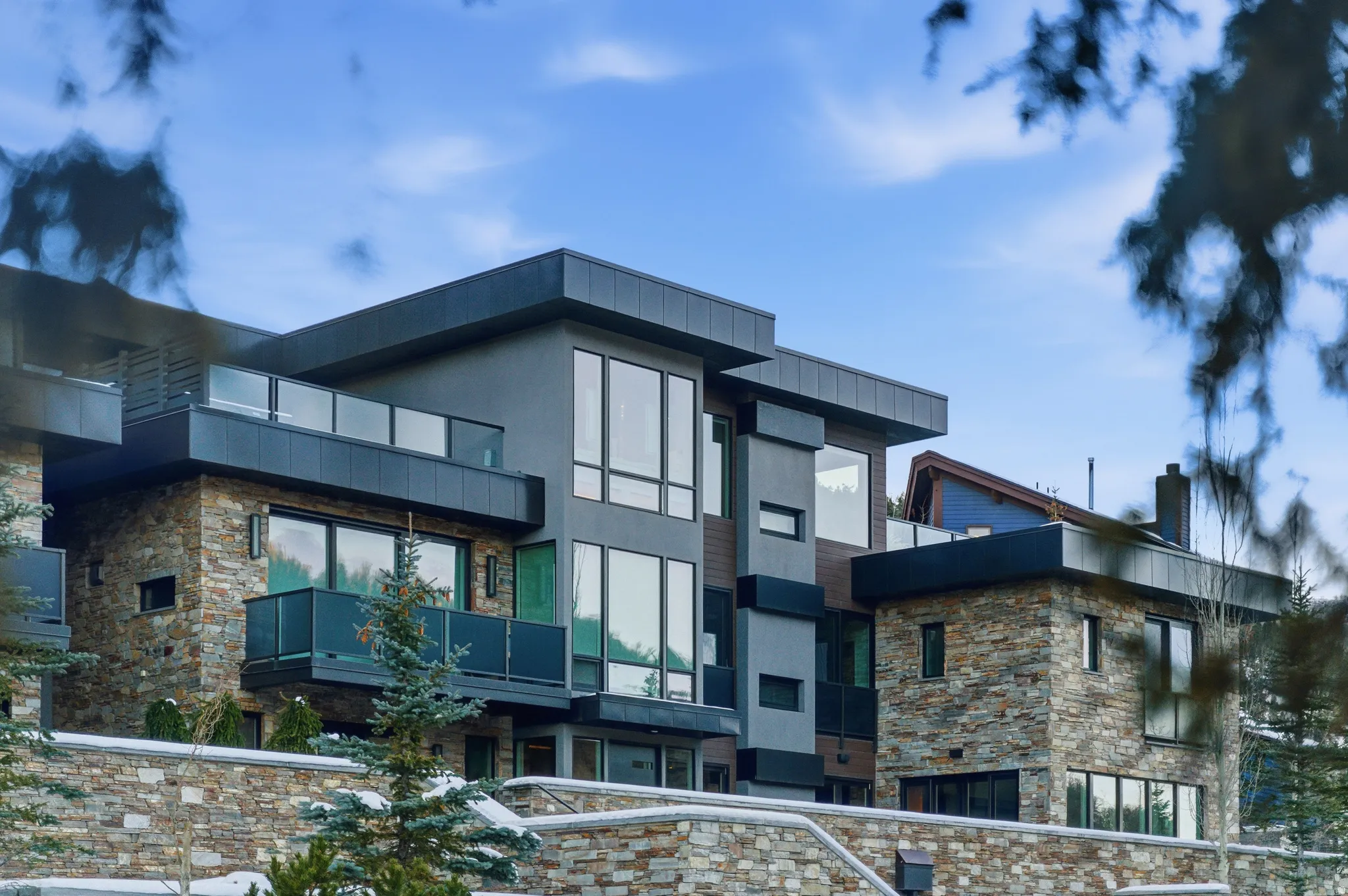 Modern exterior featuring multiple balconies with glass railings, stone veneer accents, flat rooflines, and extensive window placements