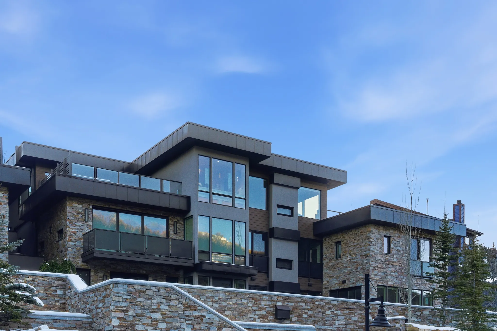 Modern multi-level exterior with extensive stonework, large pane windows, and multiple balconies featuring glass railings
