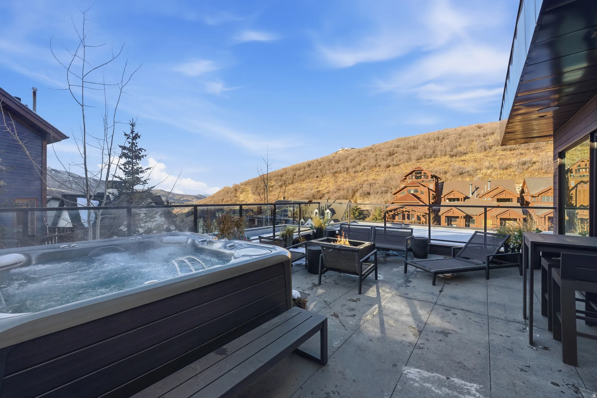Expansive rooftop deck featuring a built-in hot tub, concrete-finish flooring, and glass panel railing