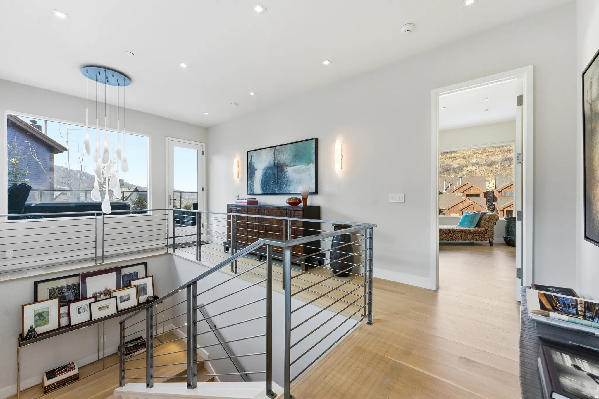 Light wood-finish flooring extends through this upper-level landing, featuring a contemporary chandelier and recessed lighting