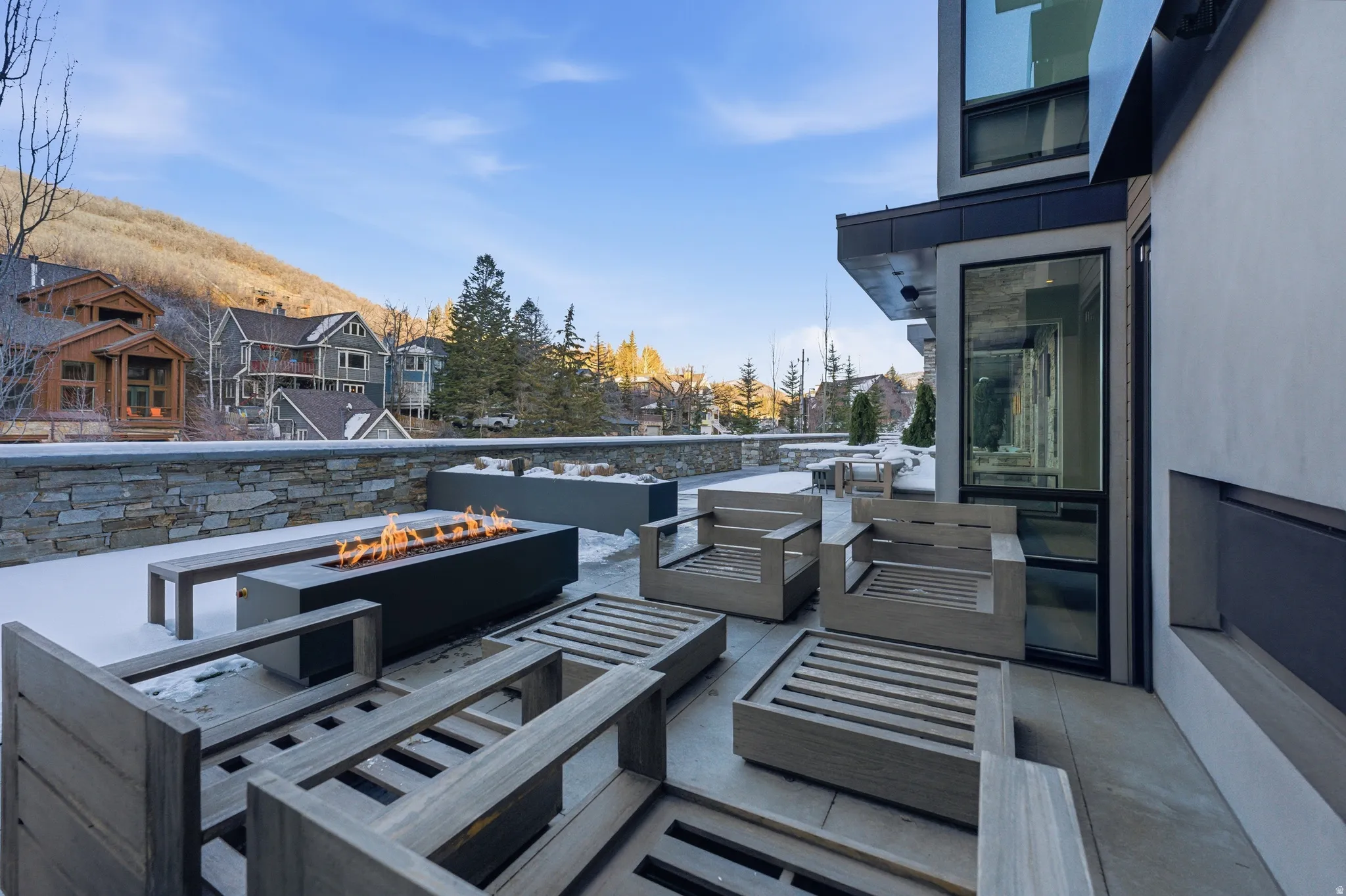 Expansive patio featuring a built-in linear fire pit, stone wall perimeter, and large format paving