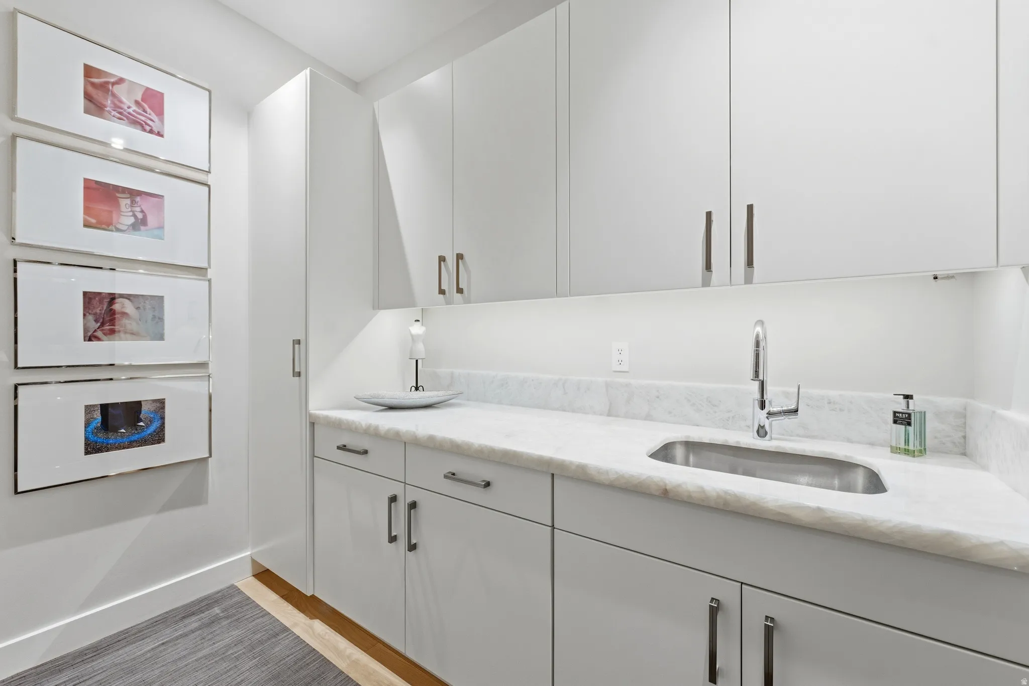 Contemporary white cabinetry with brushed nickel hardware, undermount stainless steel sink, natural stone countertop, and under-cabinet lighting