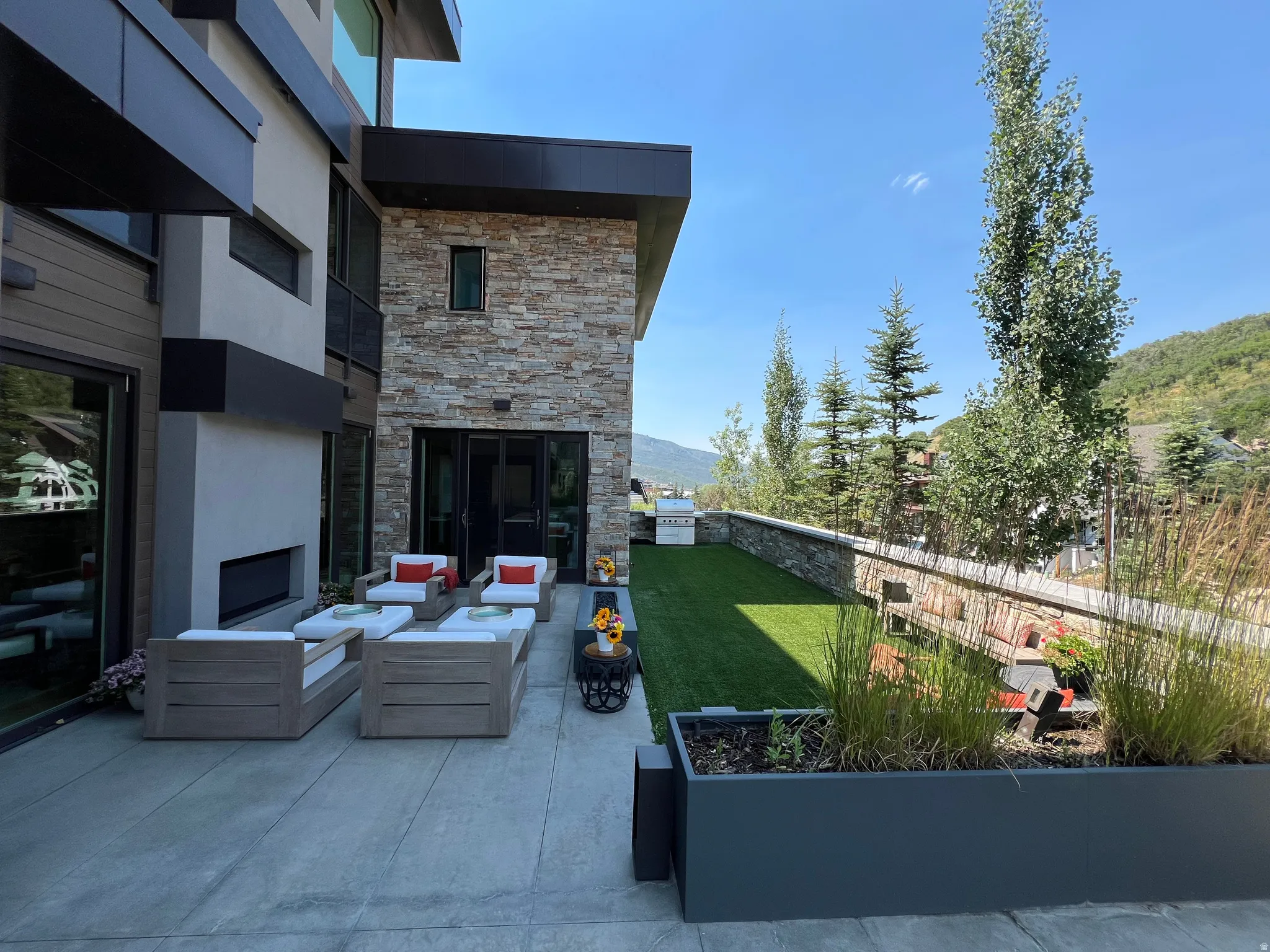 Expansive outdoor patio with a built-in fireplace, concrete flooring, and an artificial turf area