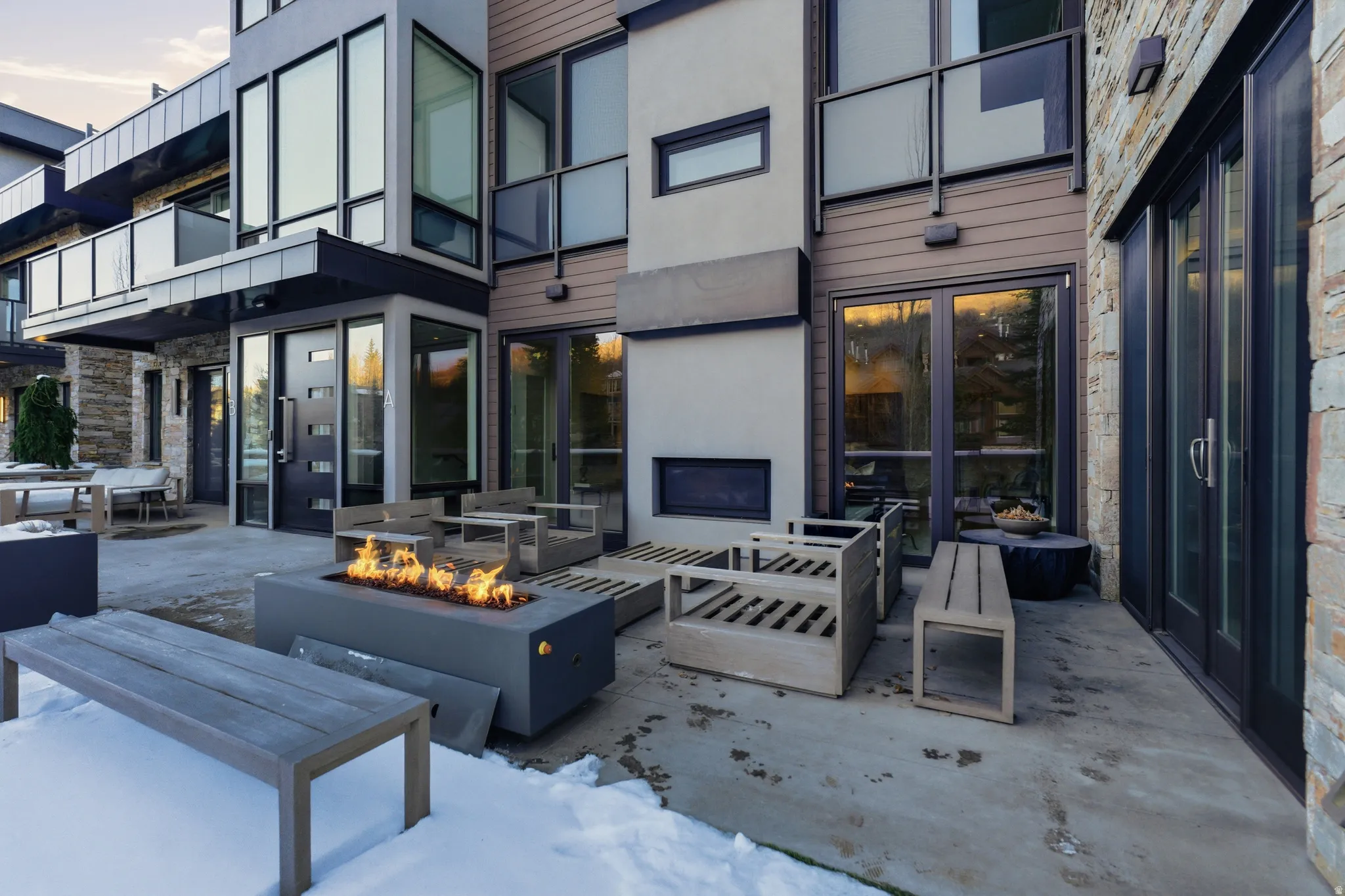 Spacious patio featuring a built-in fire pit, multiple seating areas, a stone facade, a stucco section with a built-in fireplace, and large glass doors