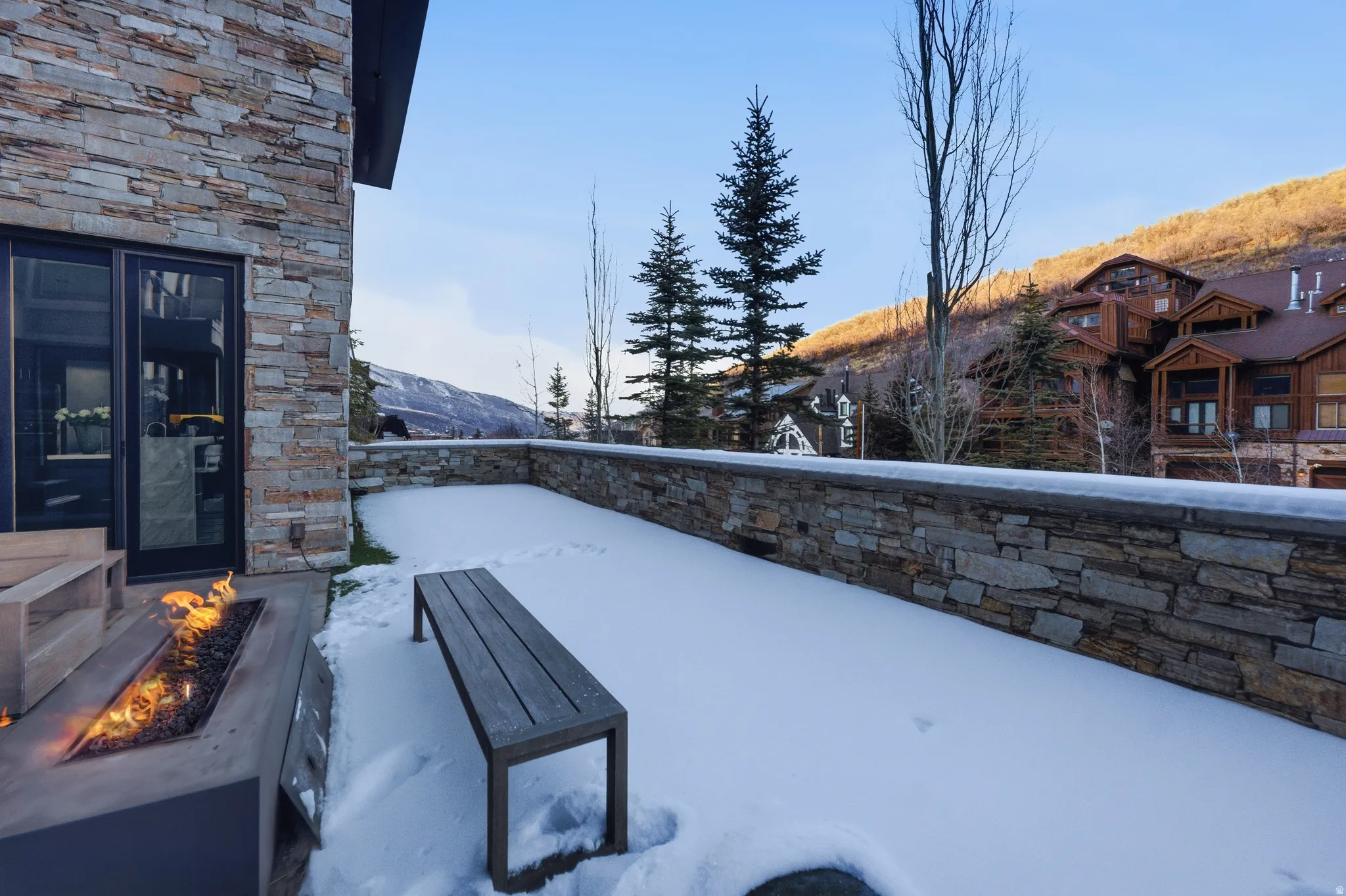 Stone-clad exterior featuring a built-in fire pit, outdoor bench, and a stone retaining wall