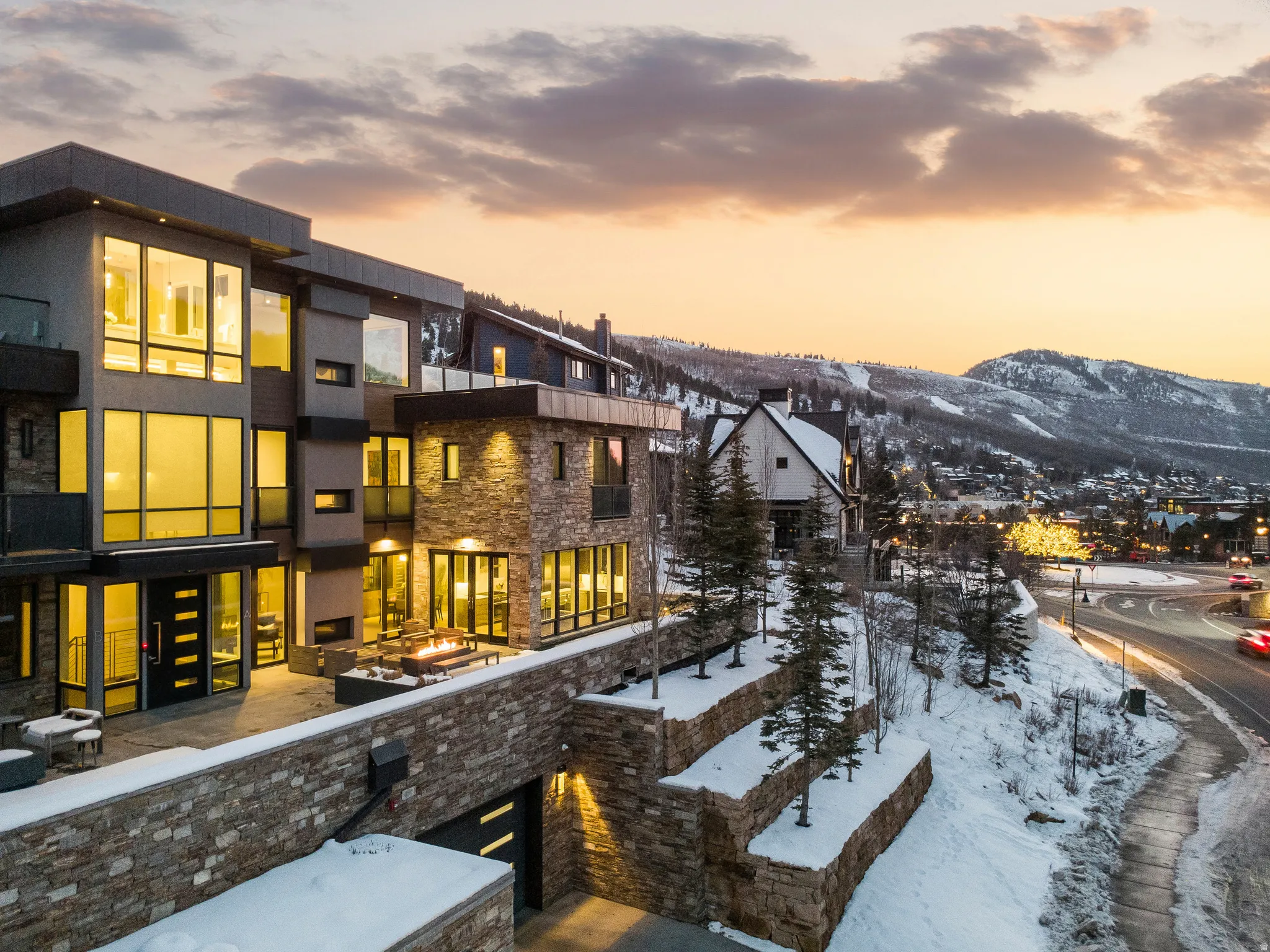 Modern multi-level residence featuring expansive windows, stone and stucco exterior finishes, and a spacious patio with a built-in fire pit