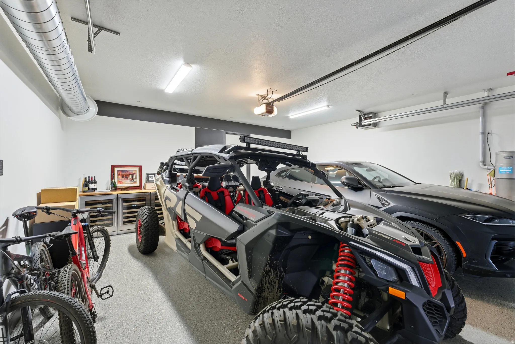 Spacious garage featuring a durable epoxy floor, exposed spiral ductwork, overhead fluorescent lighting, and built-in beverage coolers