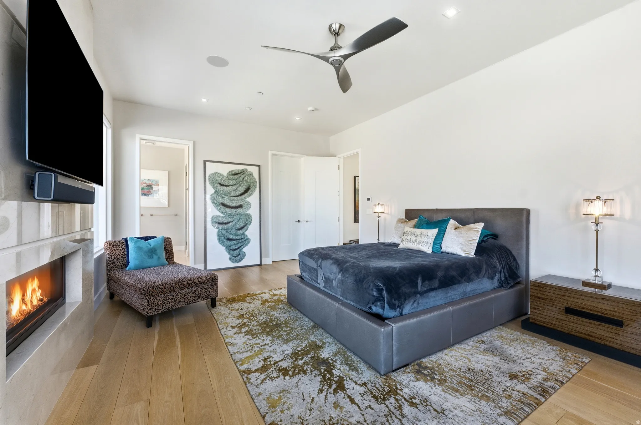 Spacious room featuring wood-finish flooring, a wall-mounted fireplace with an integrated television, and a contemporary ceiling fan