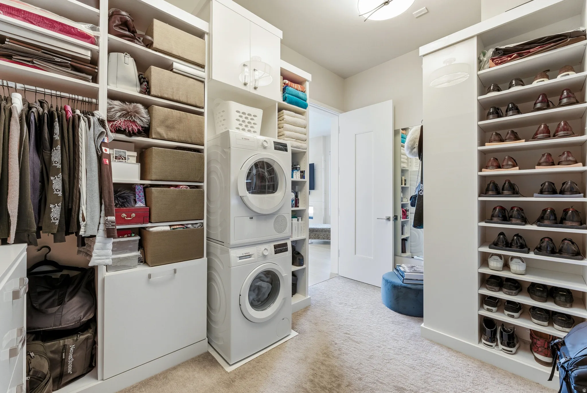 Custom closet system featuring a stacked washer and dryer, extensive shelving, hanging rods, and integrated shoe storage