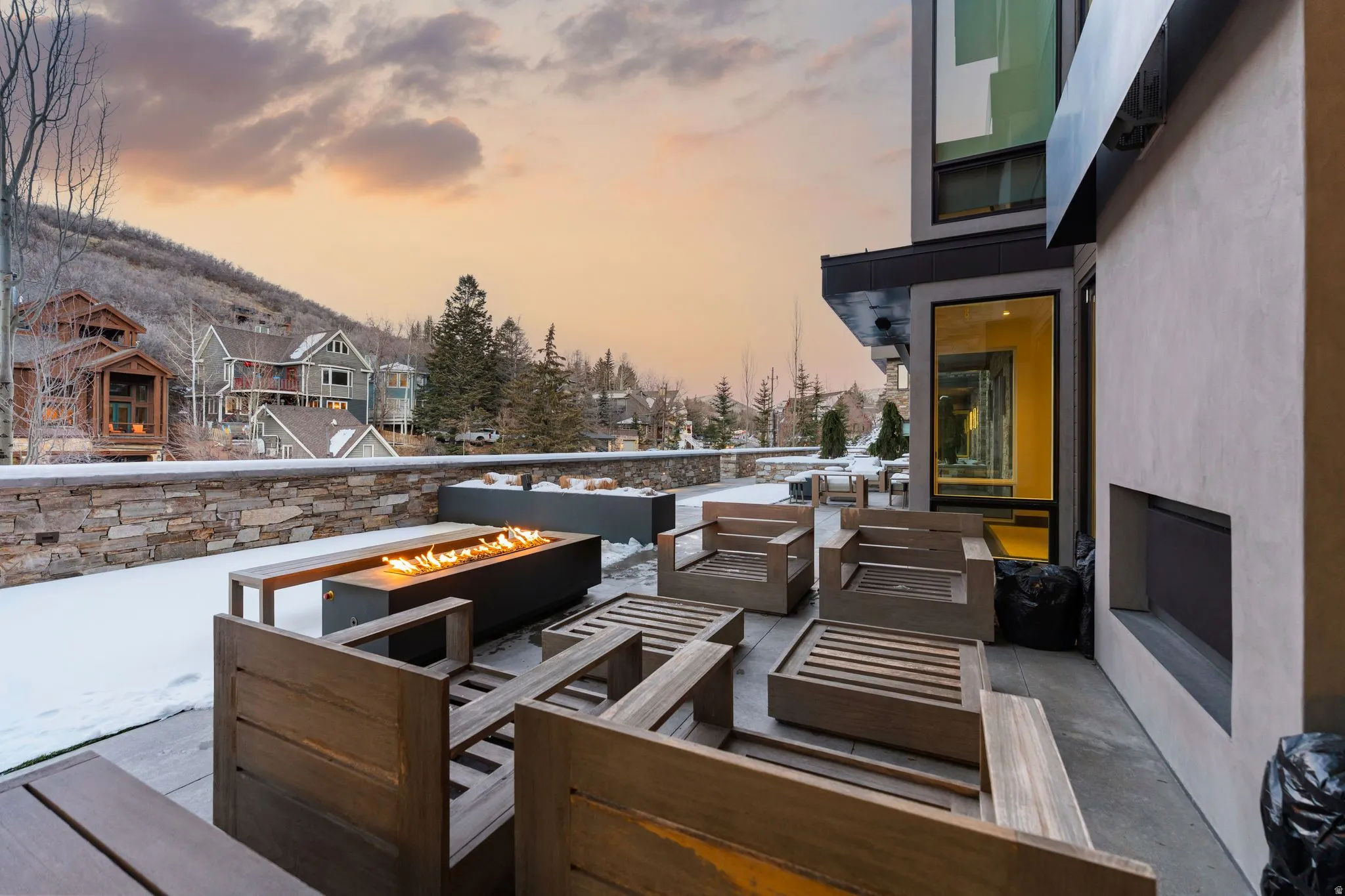 Expansive outdoor patio featuring a linear fire pit, stone retaining wall, and a large built-in outdoor fireplace