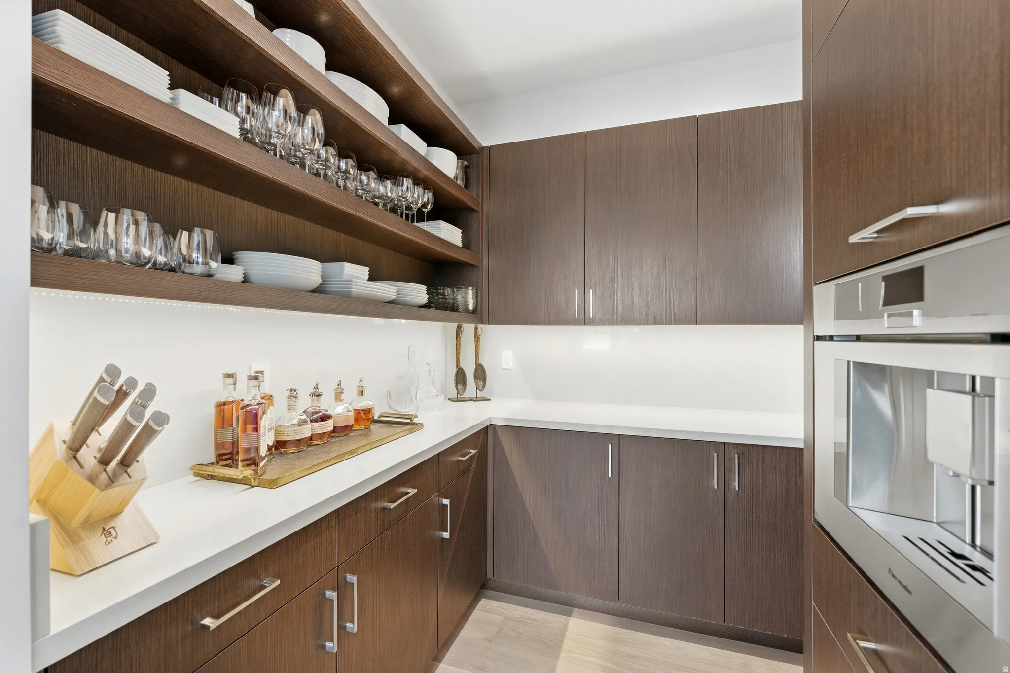 Kitchen featuring built-in stainless steel appliances, extensive wood-finish cabinetry, open shelving, white countertops, and under-cabinet lighting