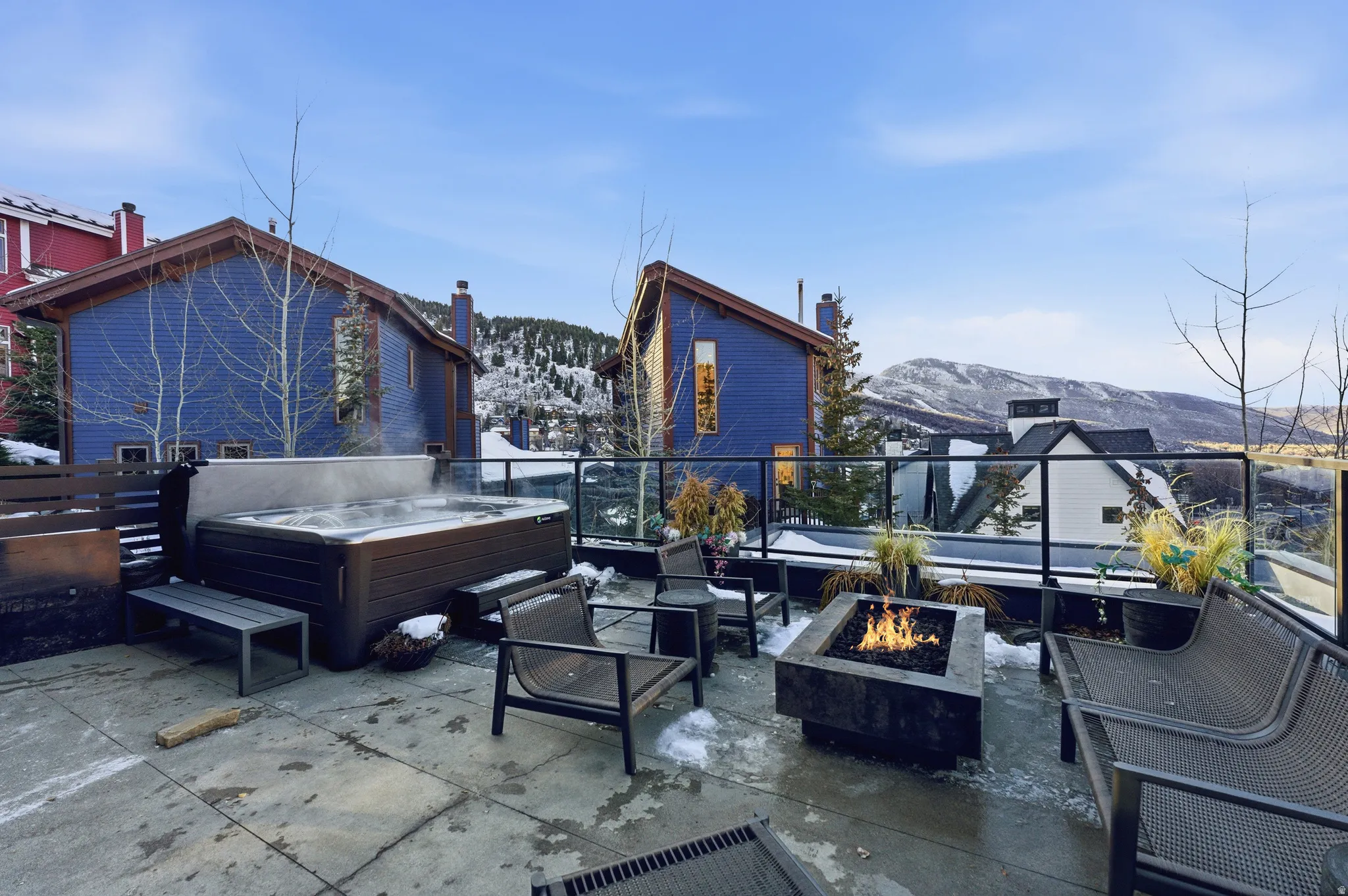 Spacious outdoor patio featuring a hot tub, a built-in fire pit, and a glass-paneled railing