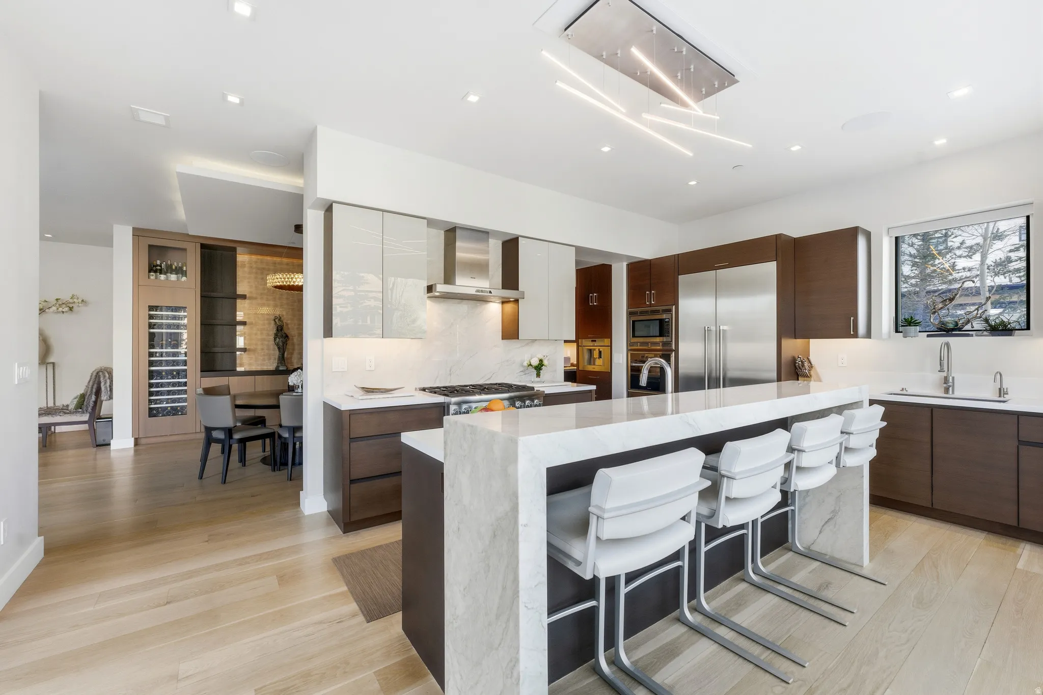 Gourmet kitchen featuring a large central island with seating, integrated stainless steel appliances, wood-finish flooring, and a built-in wine cooler
