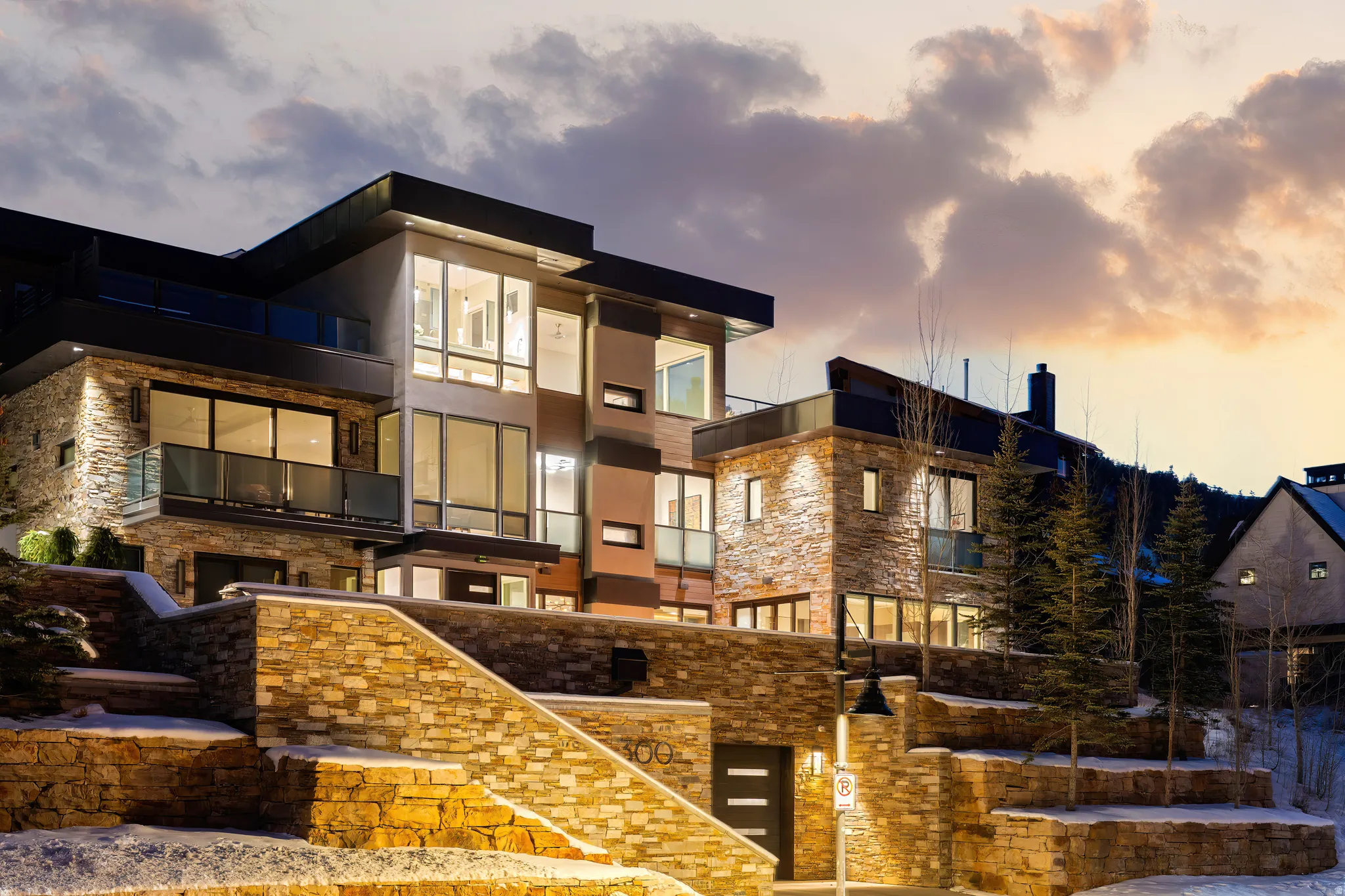 Multi-level modern residence featuring extensive stone veneer siding, large pane windows, and multiple private balconies with glass railings