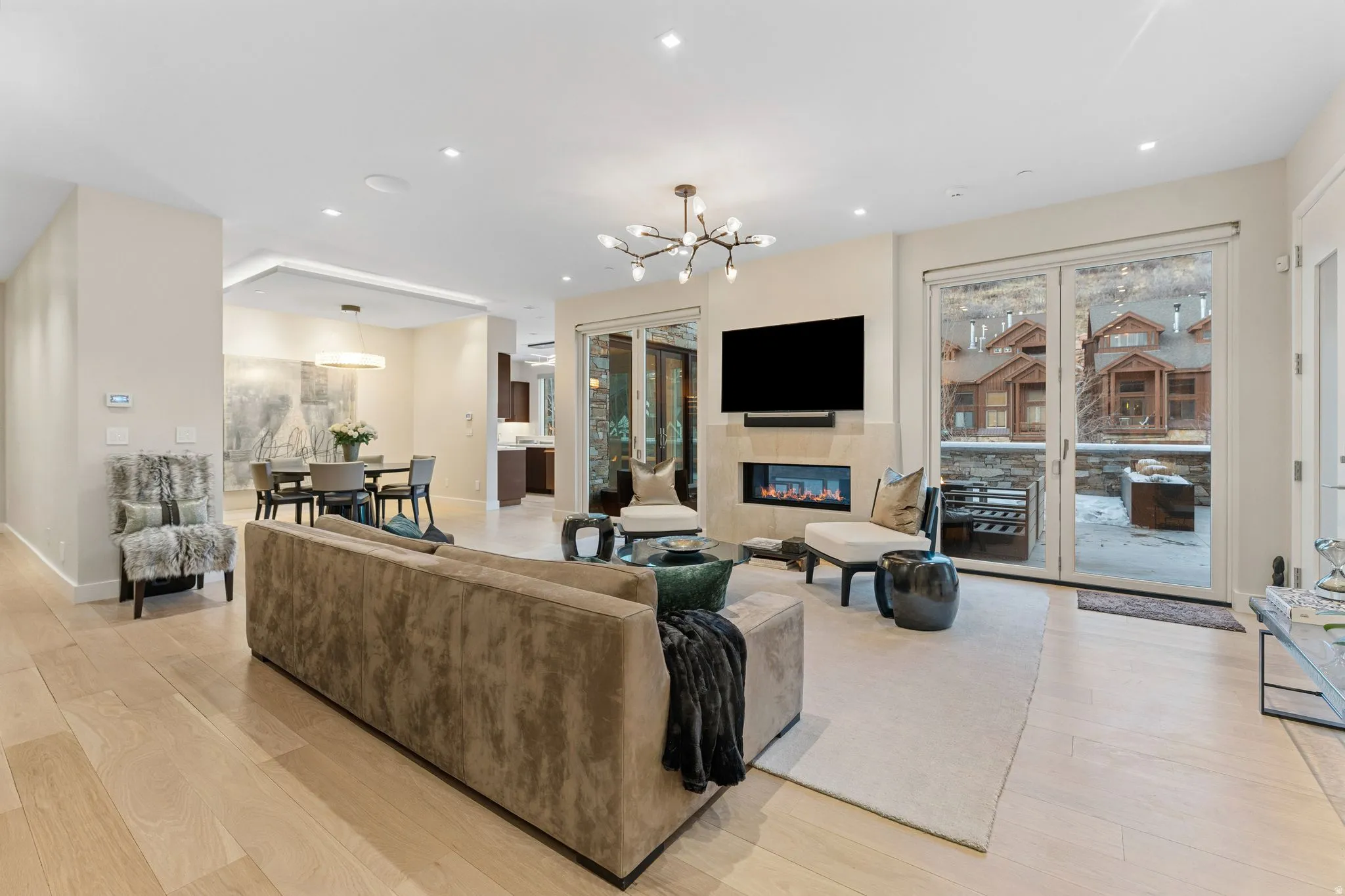 Spacious living area featuring light wood-finish flooring, a modern linear fireplace, and direct patio access through glass doors