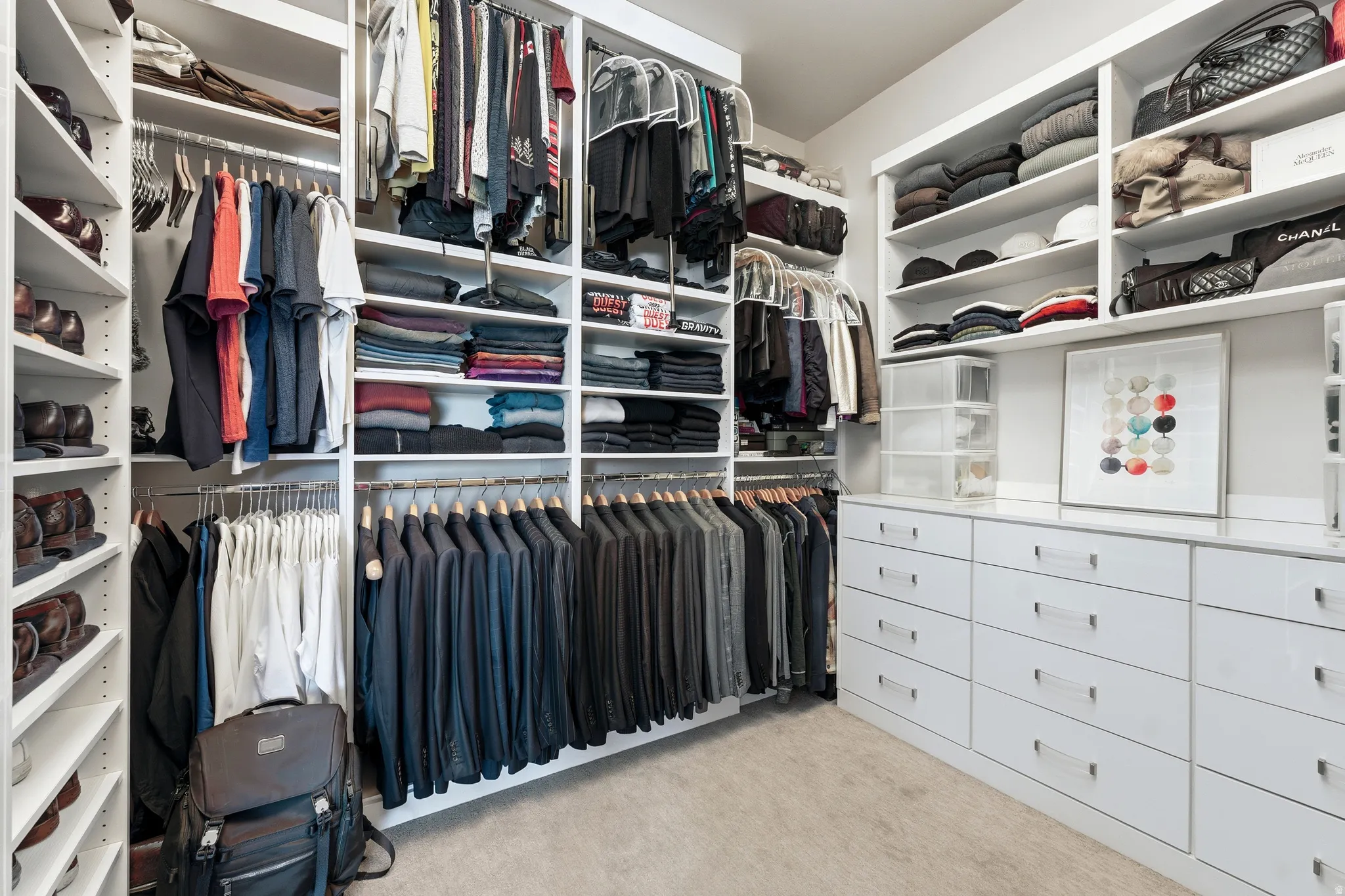 Custom closet system featuring extensive built-in shelving, multiple hanging rods, integrated drawer storage, and a light-colored carpeted floor