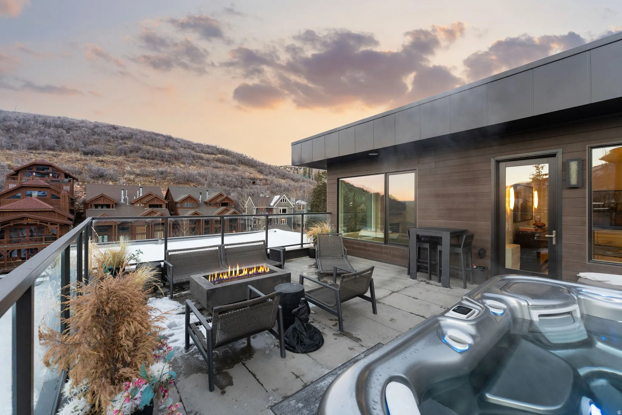 Rooftop patio featuring a built-in hot tub, linear fire pit, glass railing, and dark wood-look siding