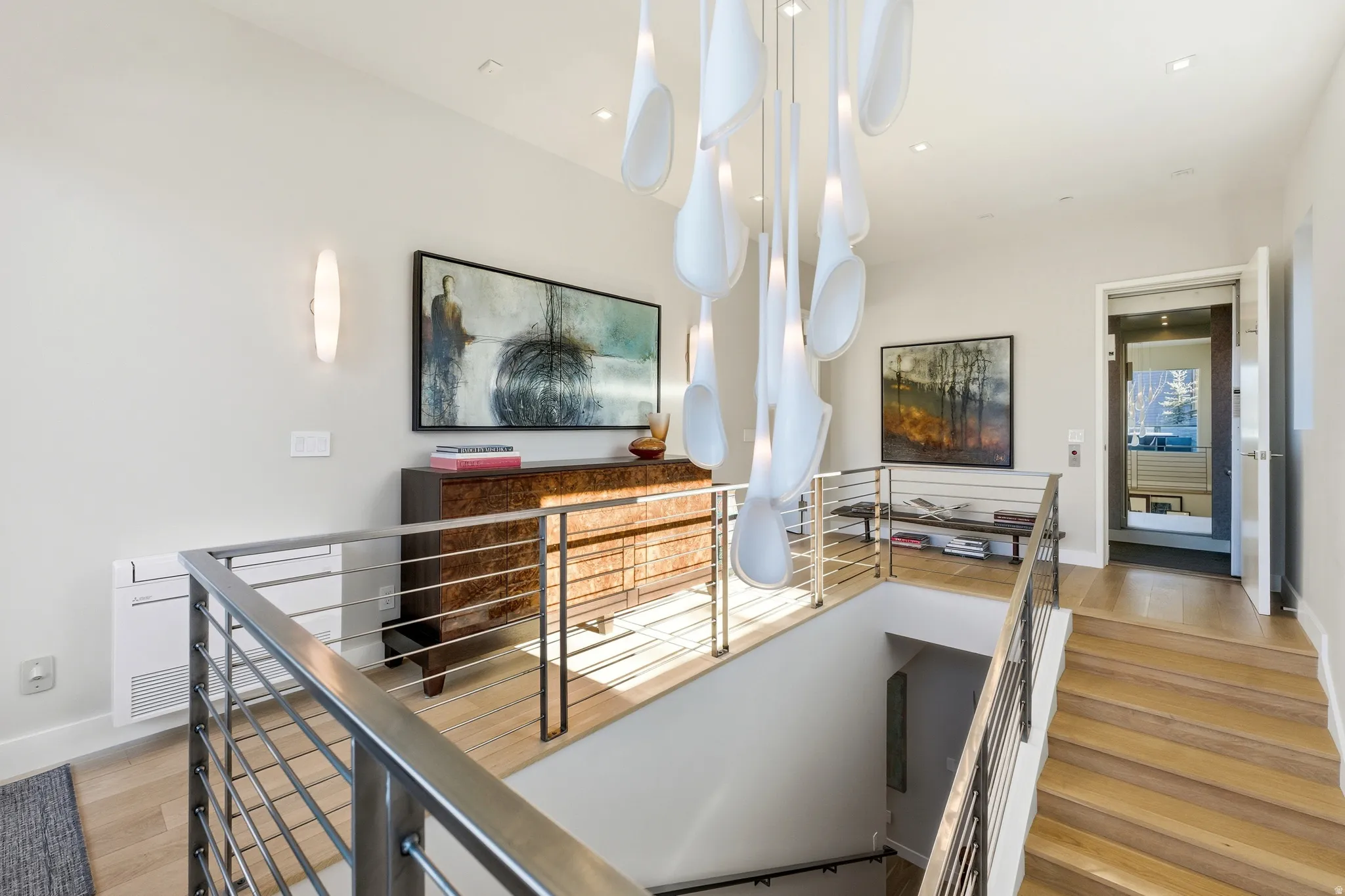 Upper landing featuring a contemporary chandelier, hardwood flooring, and stainless steel cable railings