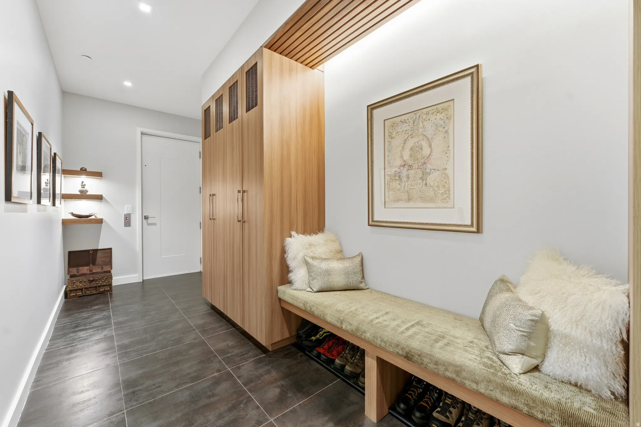 Entryway featuring dark large-format tile flooring, a built-in light wood storage system with slatted accents, and a custom built-in bench
