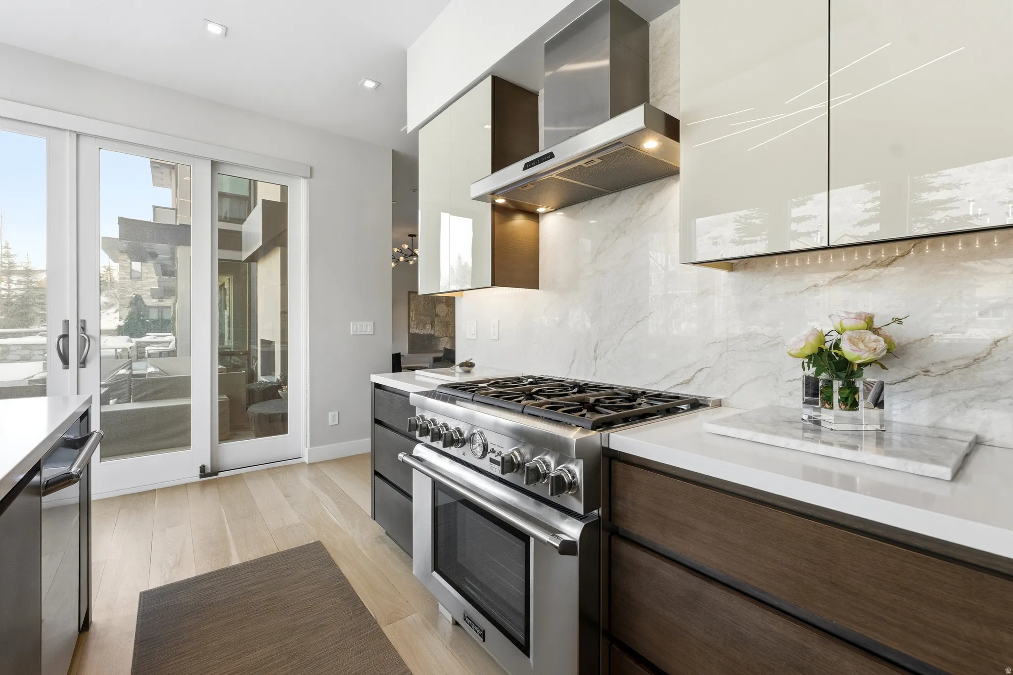 Gourmet kitchen featuring a stainless steel range with a ventilation hood, light-toned wood-finish flooring, white countertops, a stone-finish backsplash, and modern cabinetry