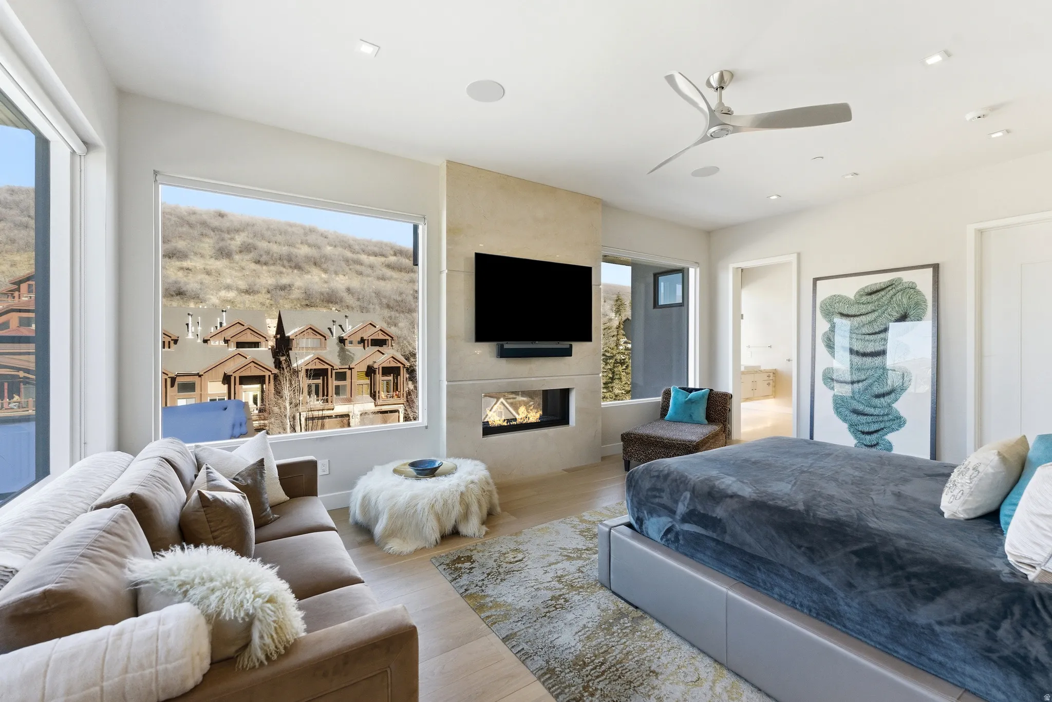 Spacious room featuring floor-to-ceiling windows, a built-in fireplace, wall-mounted television, wood-finish flooring, and a ceiling fan