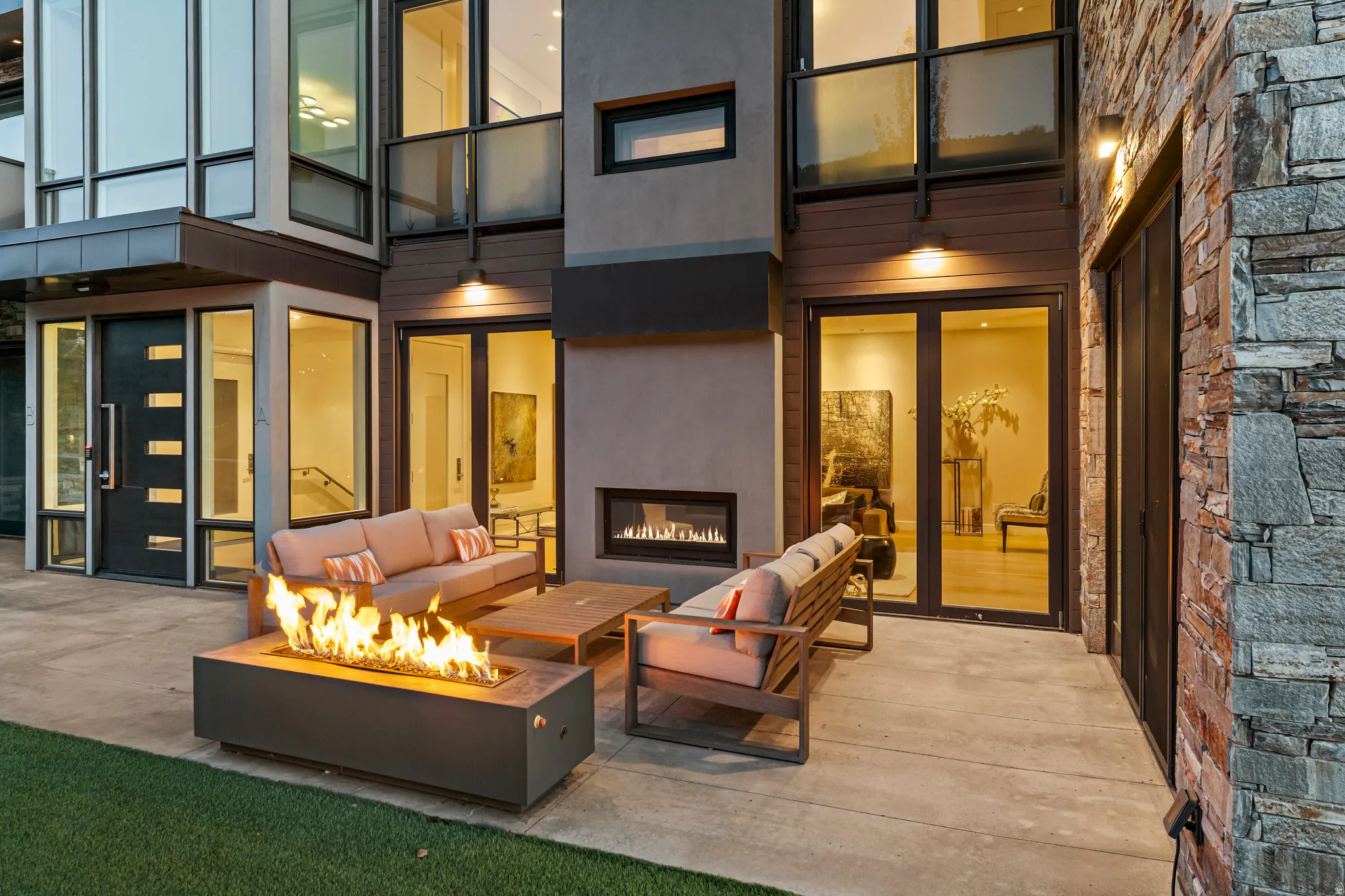 Spacious concrete patio featuring a modern fire pit, an outdoor fireplace, and multiple floor-to-ceiling windows