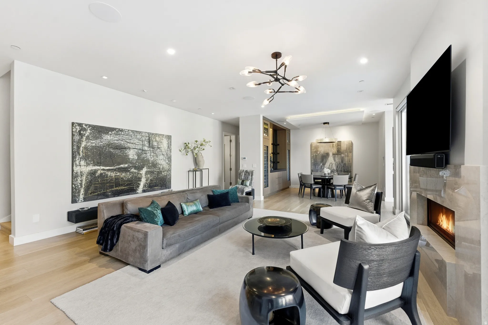 Open-concept living area featuring light wood-finish flooring, recessed lighting, and a modern chandelier