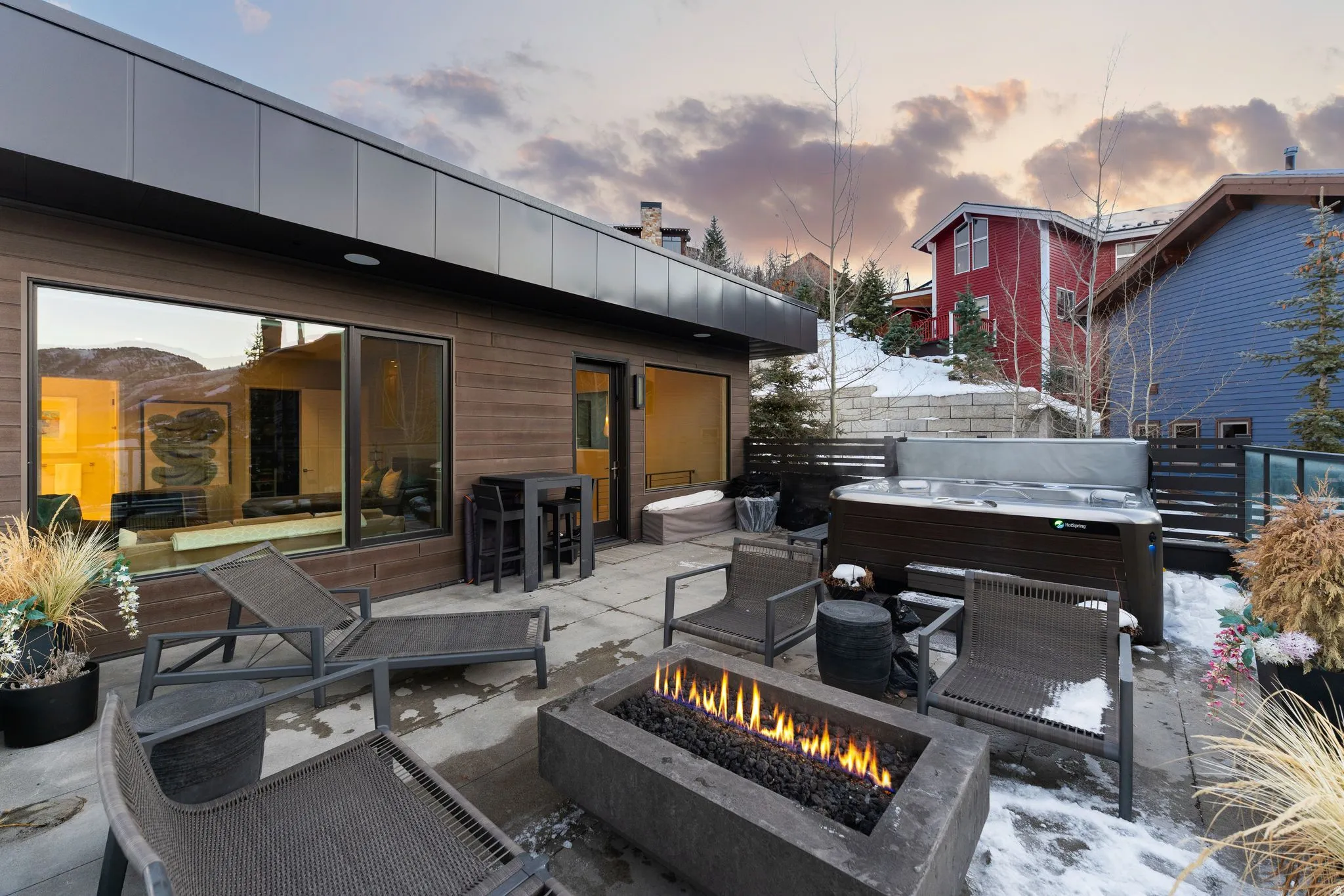 Modern outdoor patio featuring a built-in fire pit, a hot tub, and a large sliding glass door opening to the interior