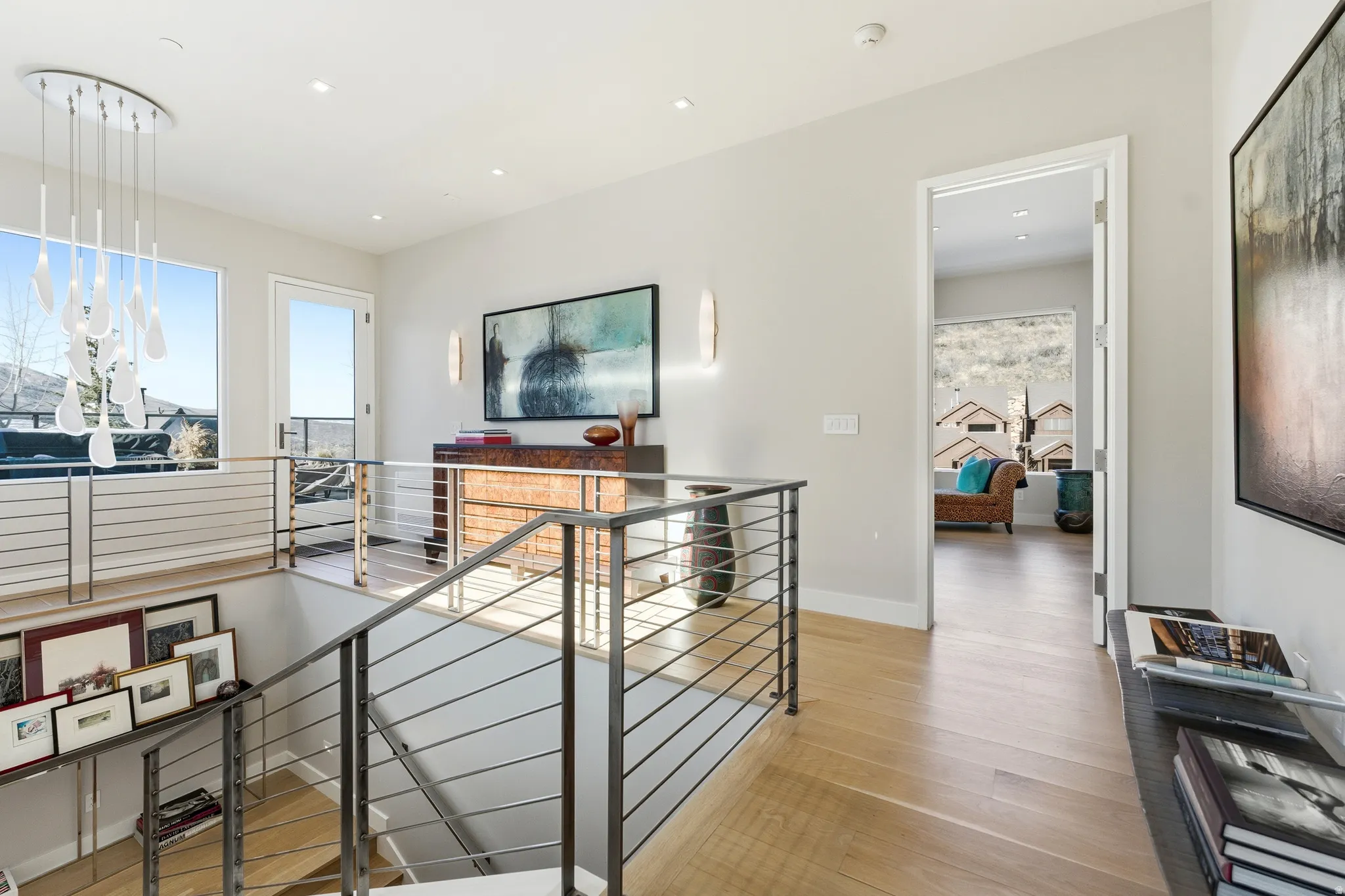 Open landing featuring light wood-finish flooring, contemporary chandelier, and cable railings