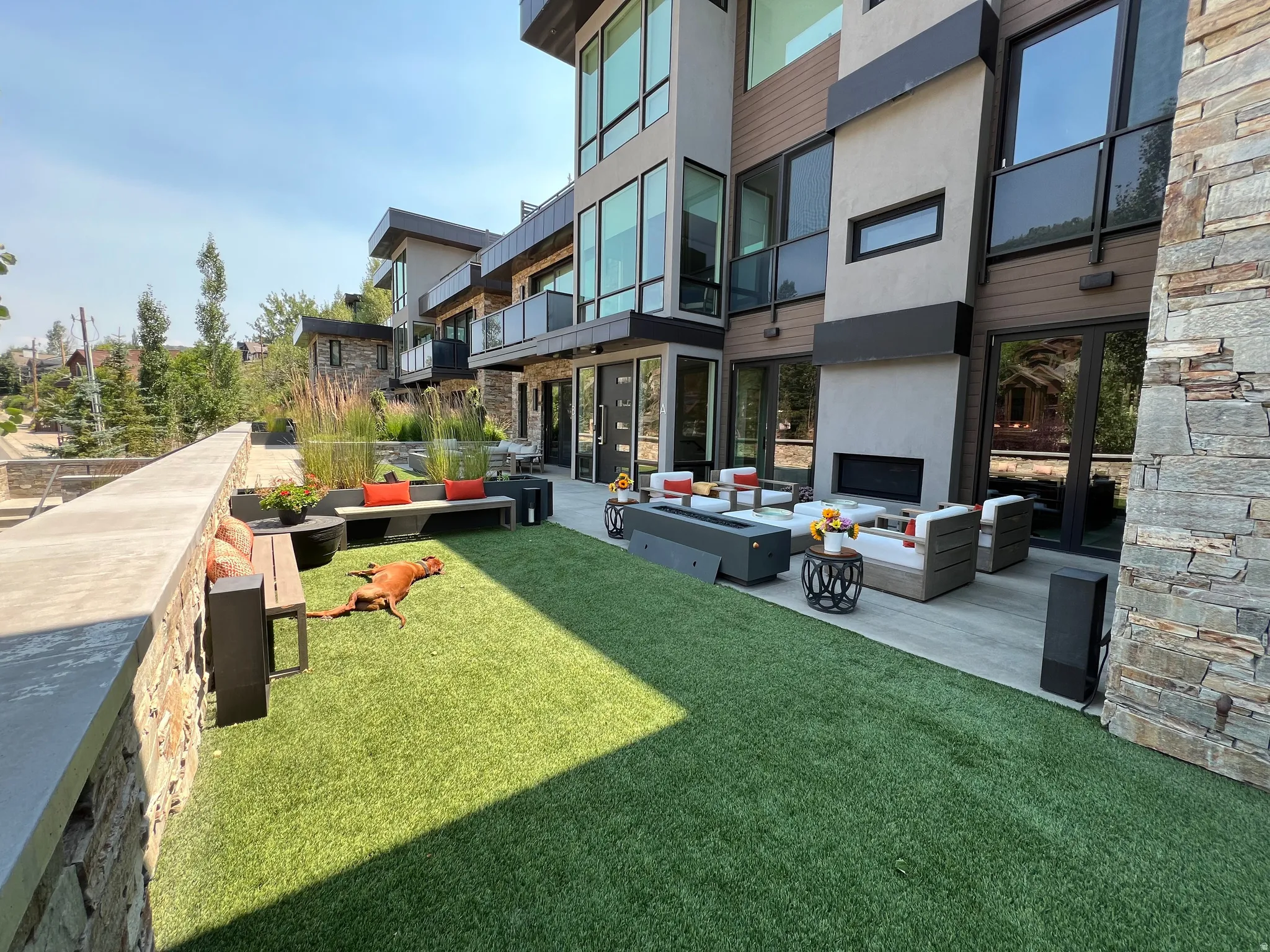 Outdoor living area featuring a stone accent wall, artificial turf lawn, and a paved patio