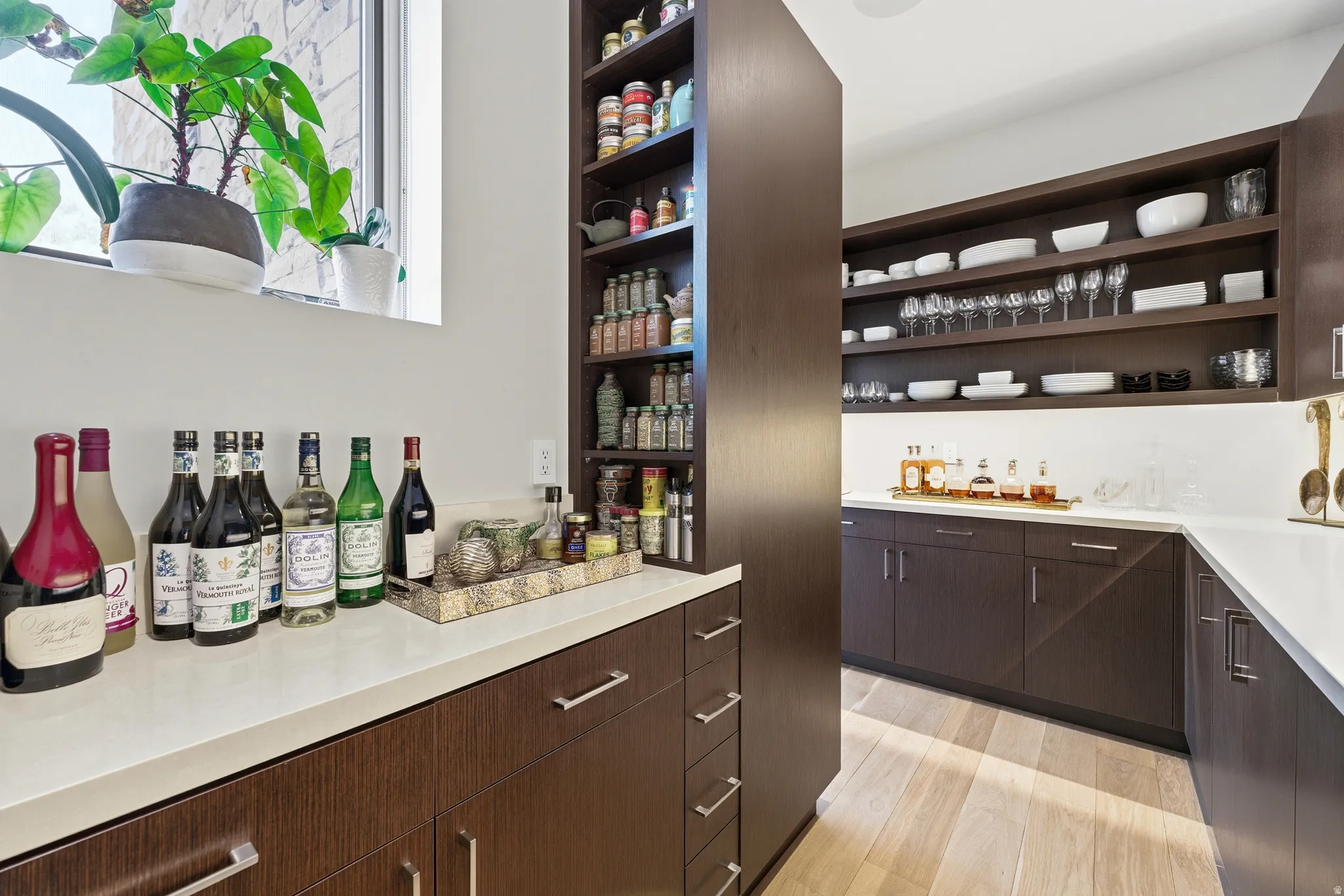 Custom pantry featuring extensive dark wood-finish cabinetry, light-toned countertops, open shelving, integrated shelving units, and a window with natural light
