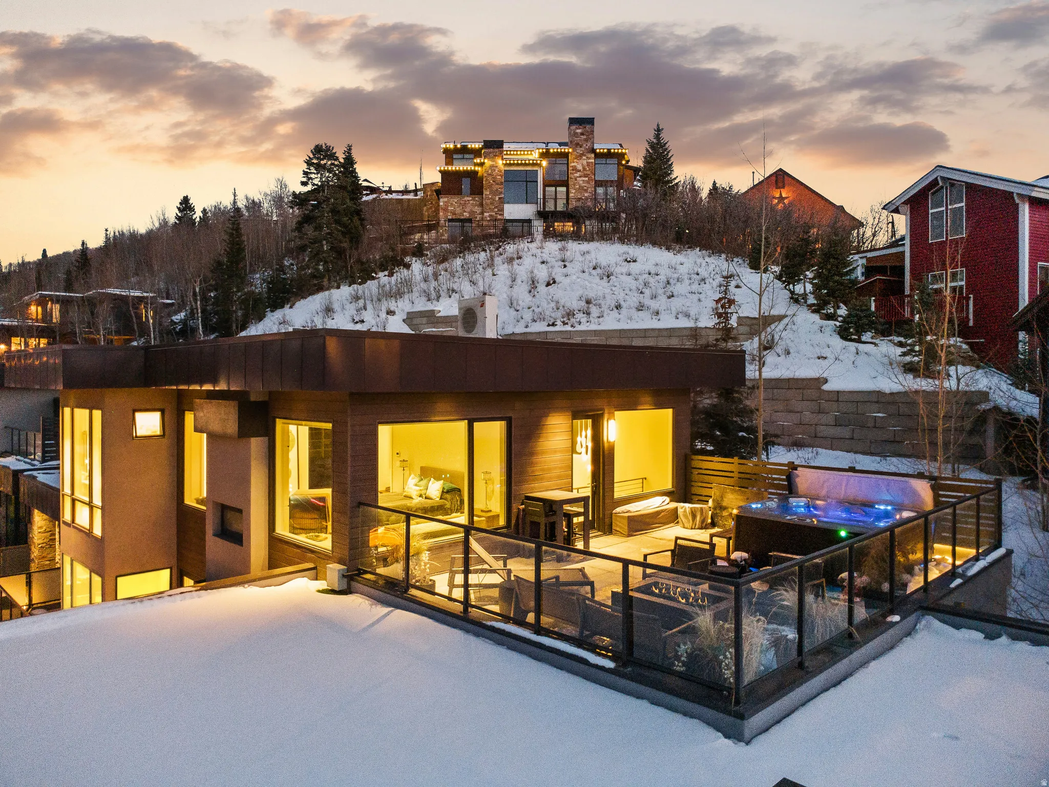 Multi-level property featuring extensive outdoor decking, a built-in spa with integrated lighting, glass panel railings, and large format windows