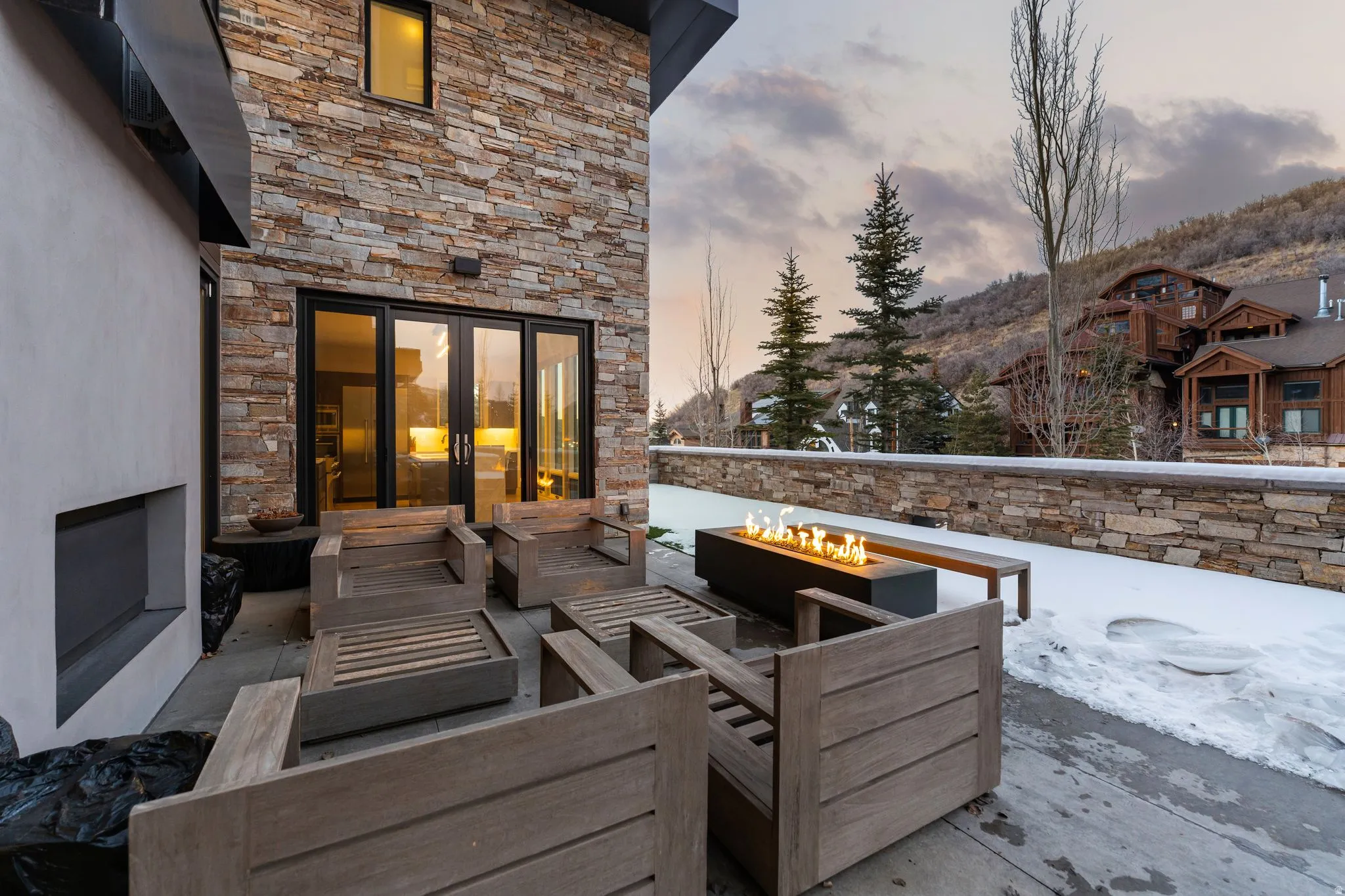 Outdoor patio featuring a built-in linear fire pit, stone accent wall, and stucco exterior