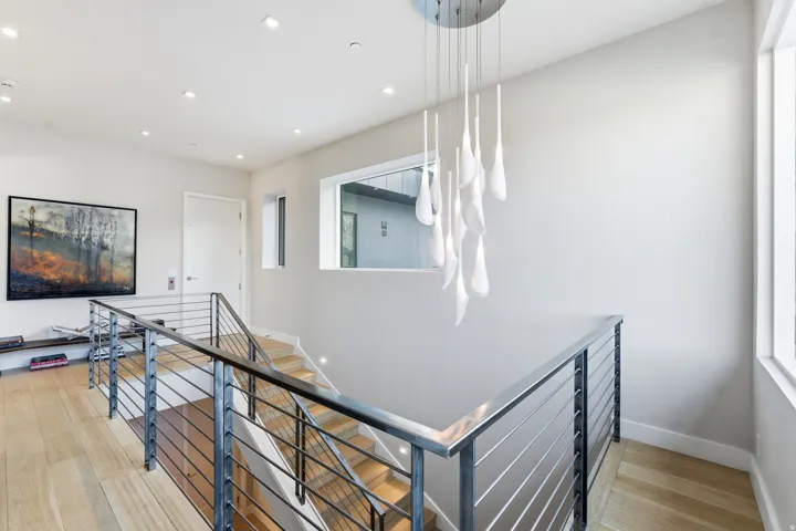 Modern staircase featuring a sleek metal railing with horizontal balusters, wood-finish flooring, and recessed ceiling lighting