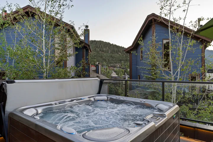 Outdoor hot tub with integrated jets and controls, set on a deck with glass panel railing