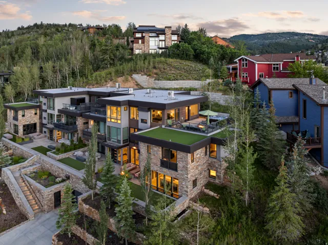 Contemporary multi-level residence featuring stone and stucco facade, multiple exterior terraces, green roof accents, and landscaped grounds with mature trees