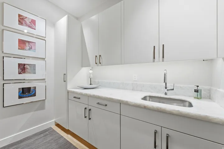 Contemporary white cabinetry with brushed nickel hardware, undermount stainless steel sink, natural stone countertop, and under-cabinet lighting